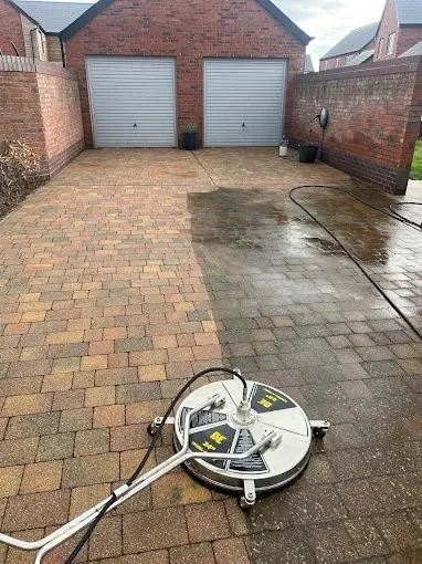 Outdoor brick driveway or patio with a robotic cleaning machine in the foreground, wet surface, and garage doors in the background.