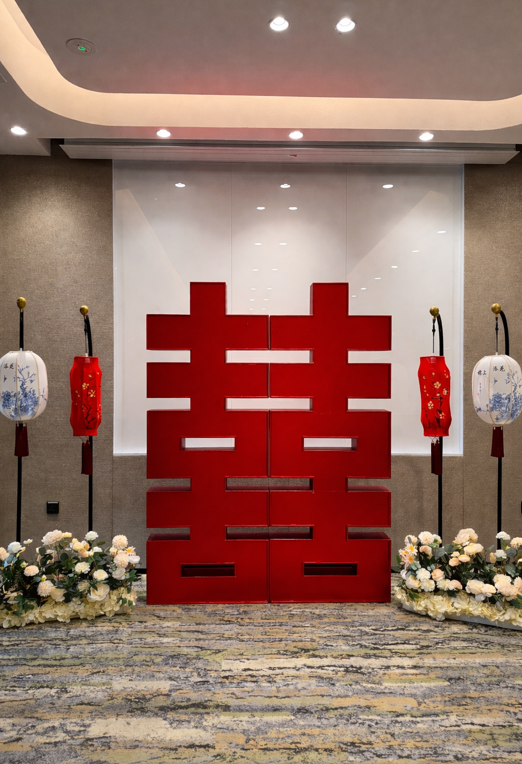 Large red Chinese character decoration flanked by traditional Chinese lanterns and floral arrangements inside a decorated room.