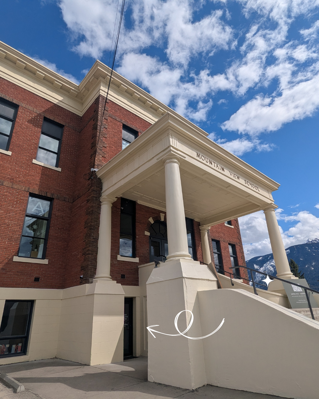Front view of Mountain View School, a red brick building with white columns and a sign reading 'Mountain View School,' with mountains and a partly cloudy sky in the background.