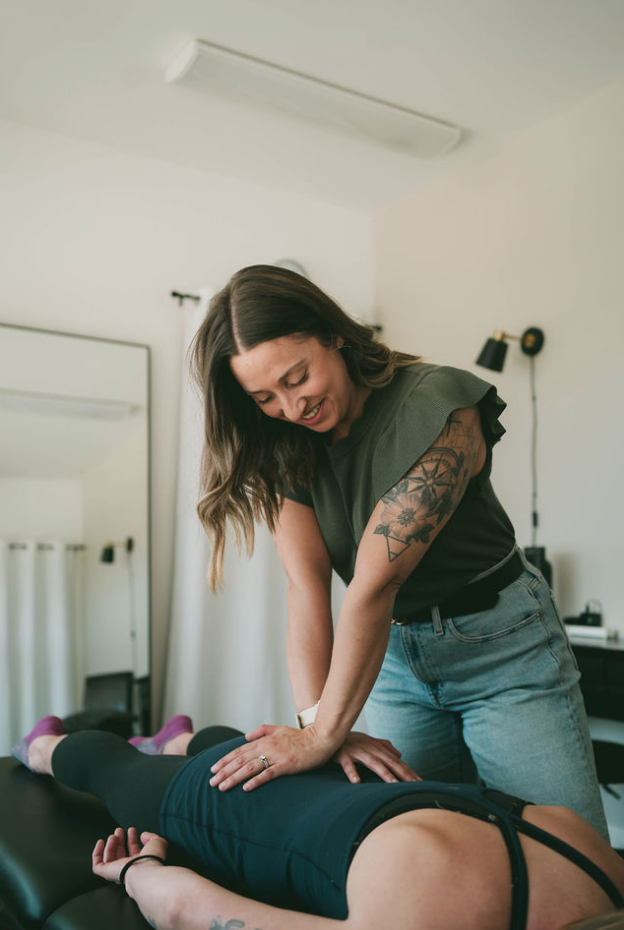 A woman giving a massage to another person lying face down on a massage table in a well-lit room.