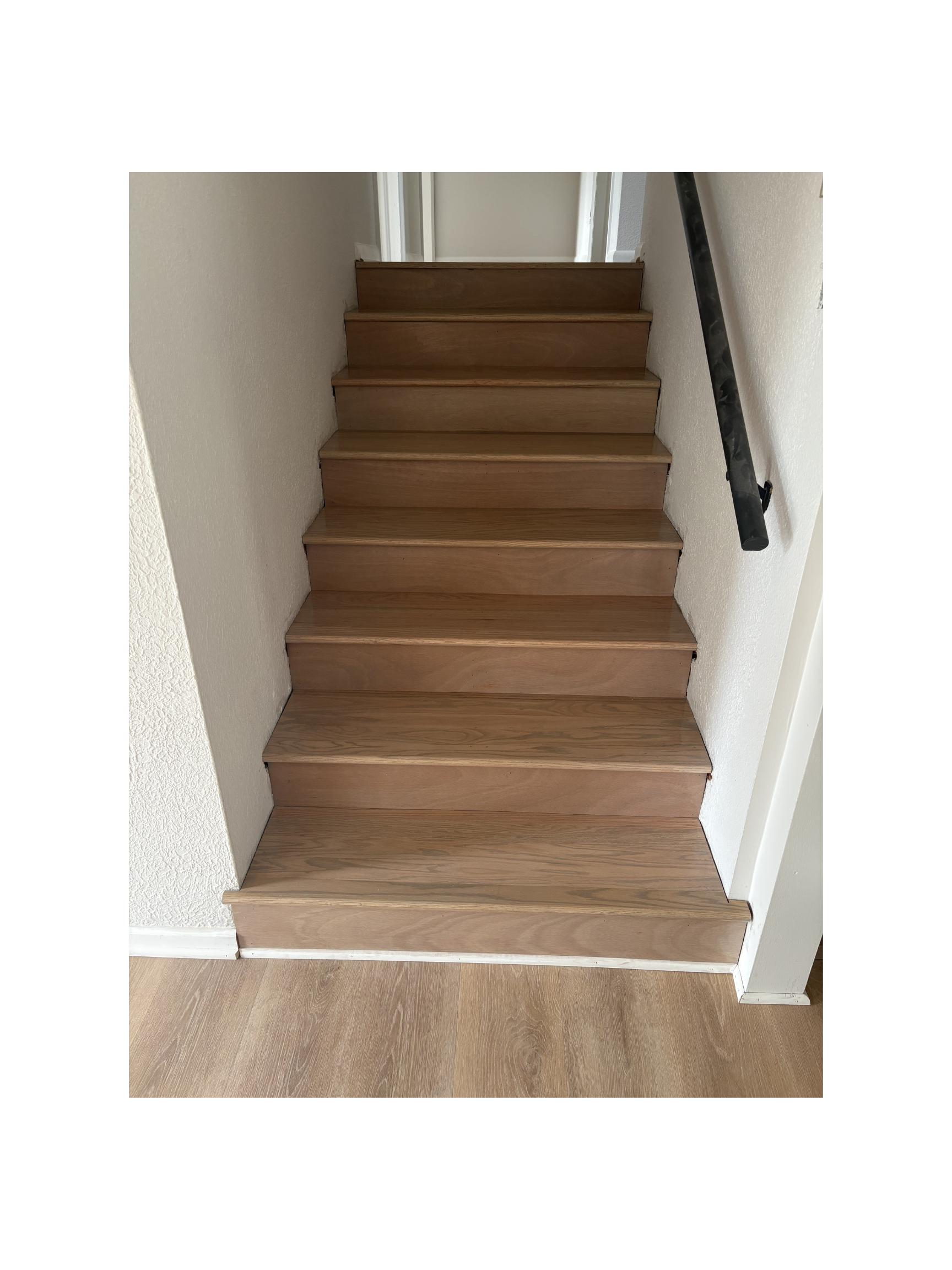 Wooden staircase with a black handrail on the right side, leading up to a landing with a door at the top.