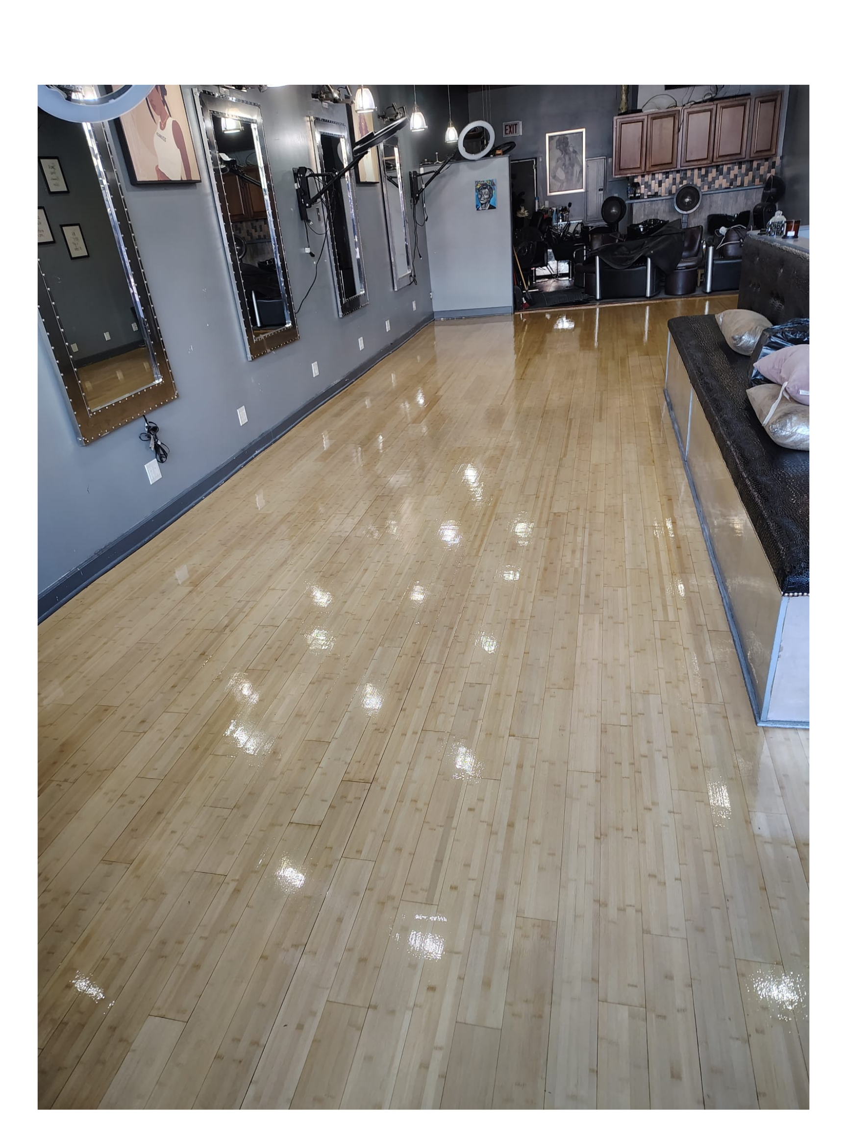 Empty salon with a shiny wooden floor, mirrors on the wall, hair styling stations, and salon chairs in the background.