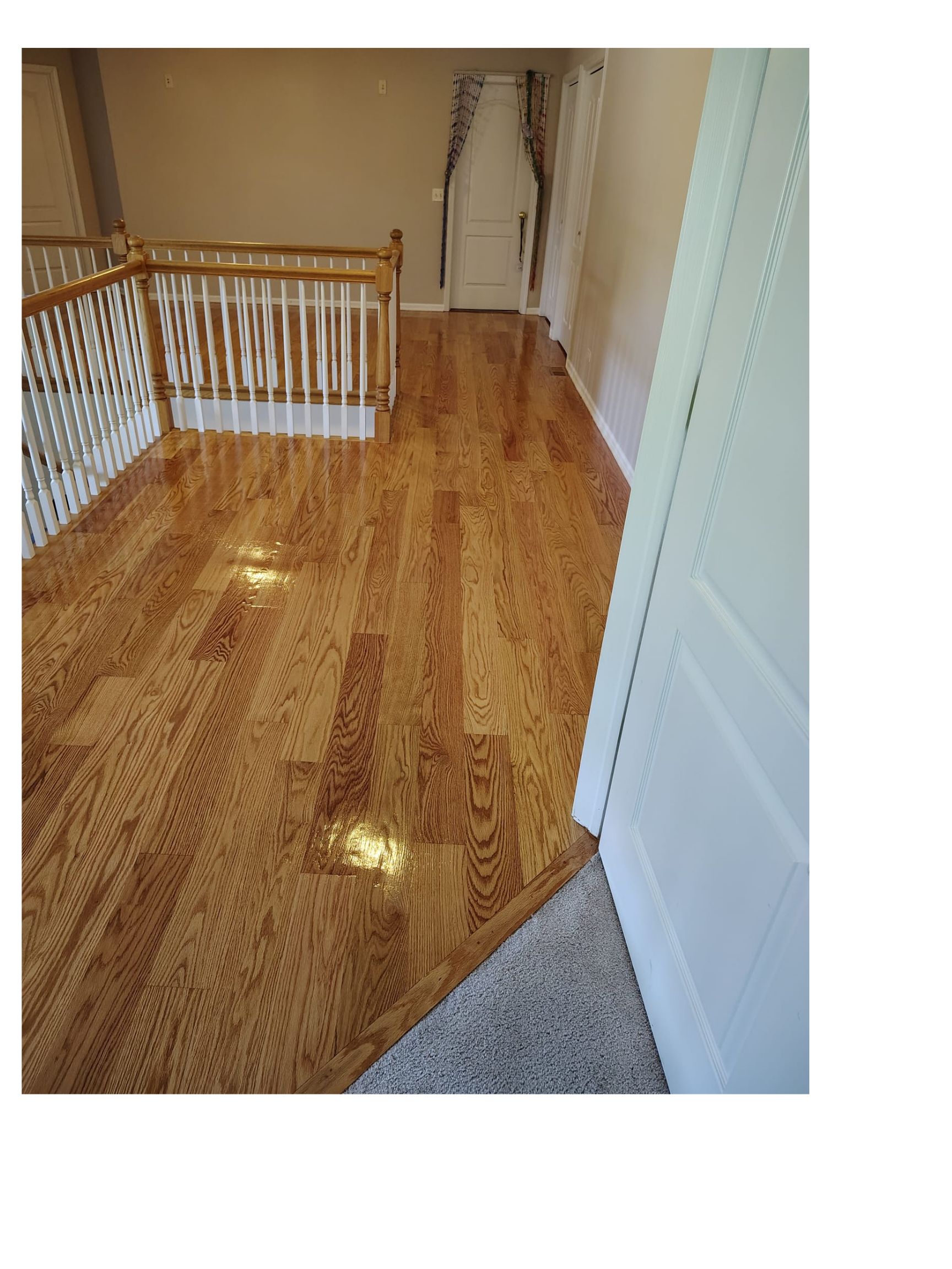 Wooden floor hallway with staircase and white doorway in a house.