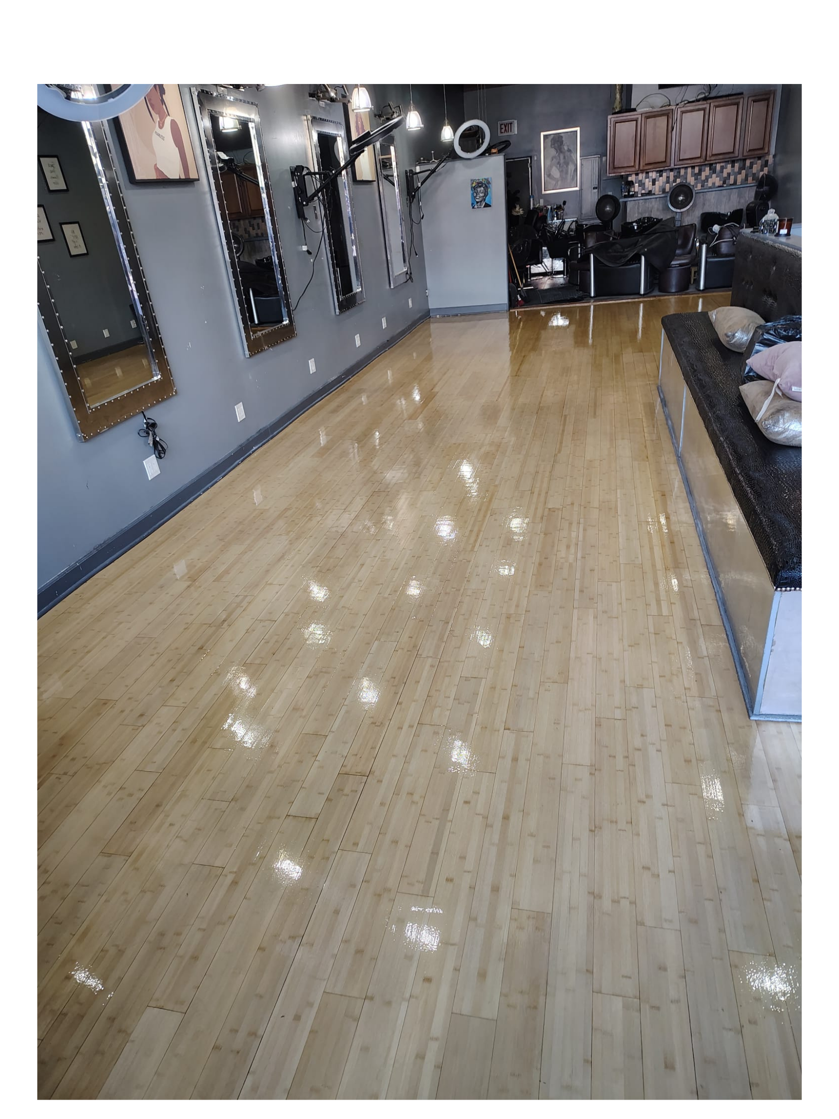 Empty salon with a shiny wooden floor, wall mirrors, salon chairs, and hairstyle pictures