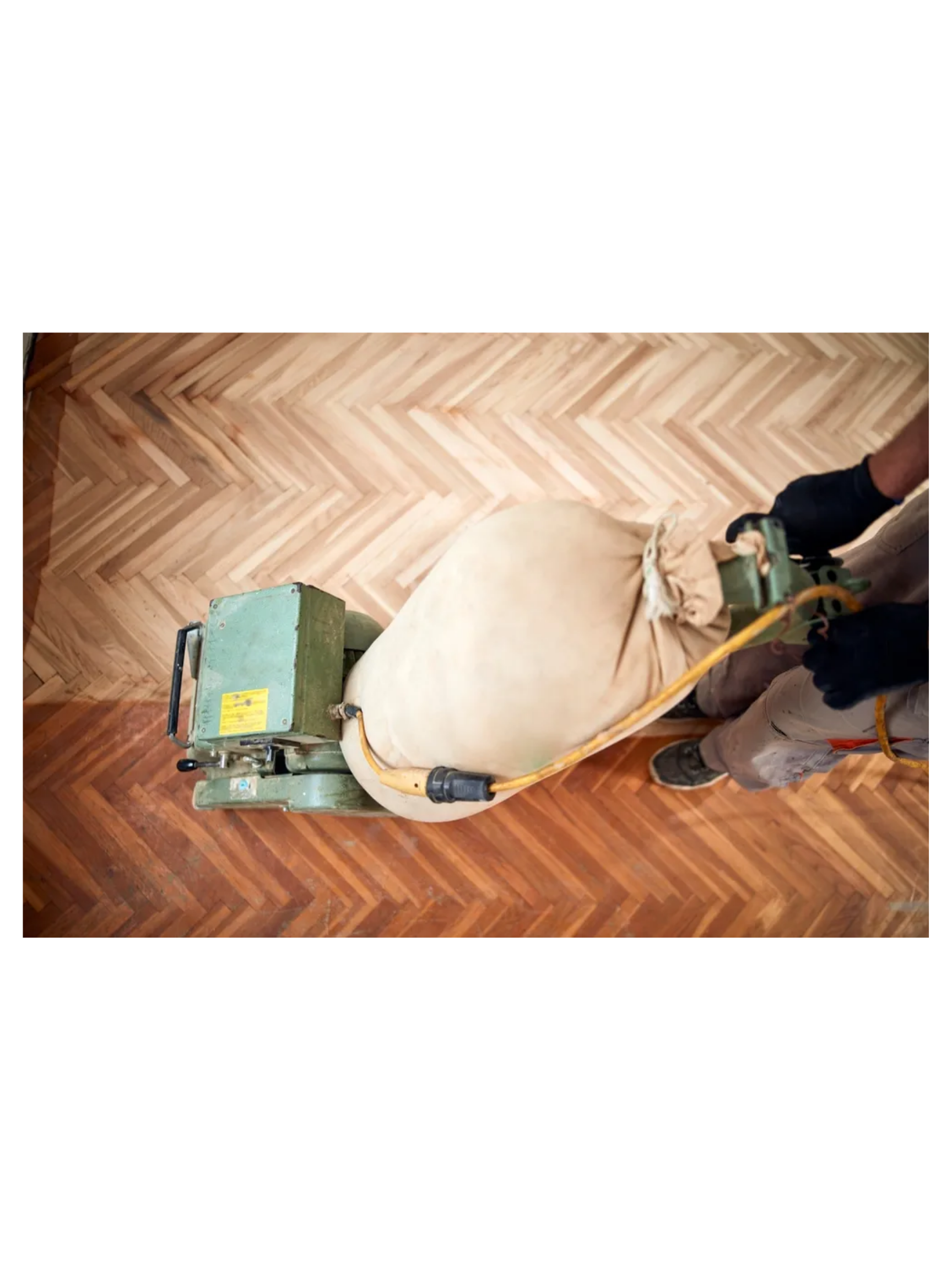 A person using a floor sanders to polish a herringbone wood floor.