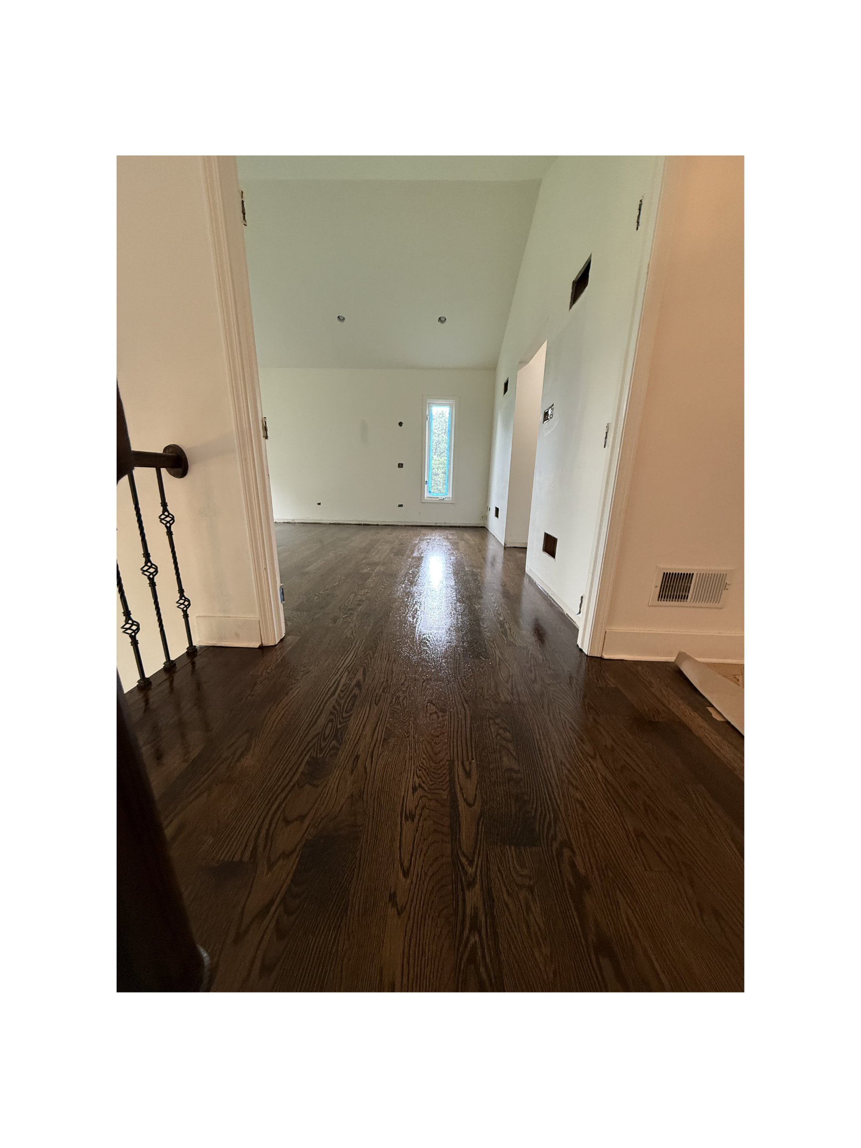 Empty room with wooden floors, white walls, and a narrow window at the back, under construction or renovation.