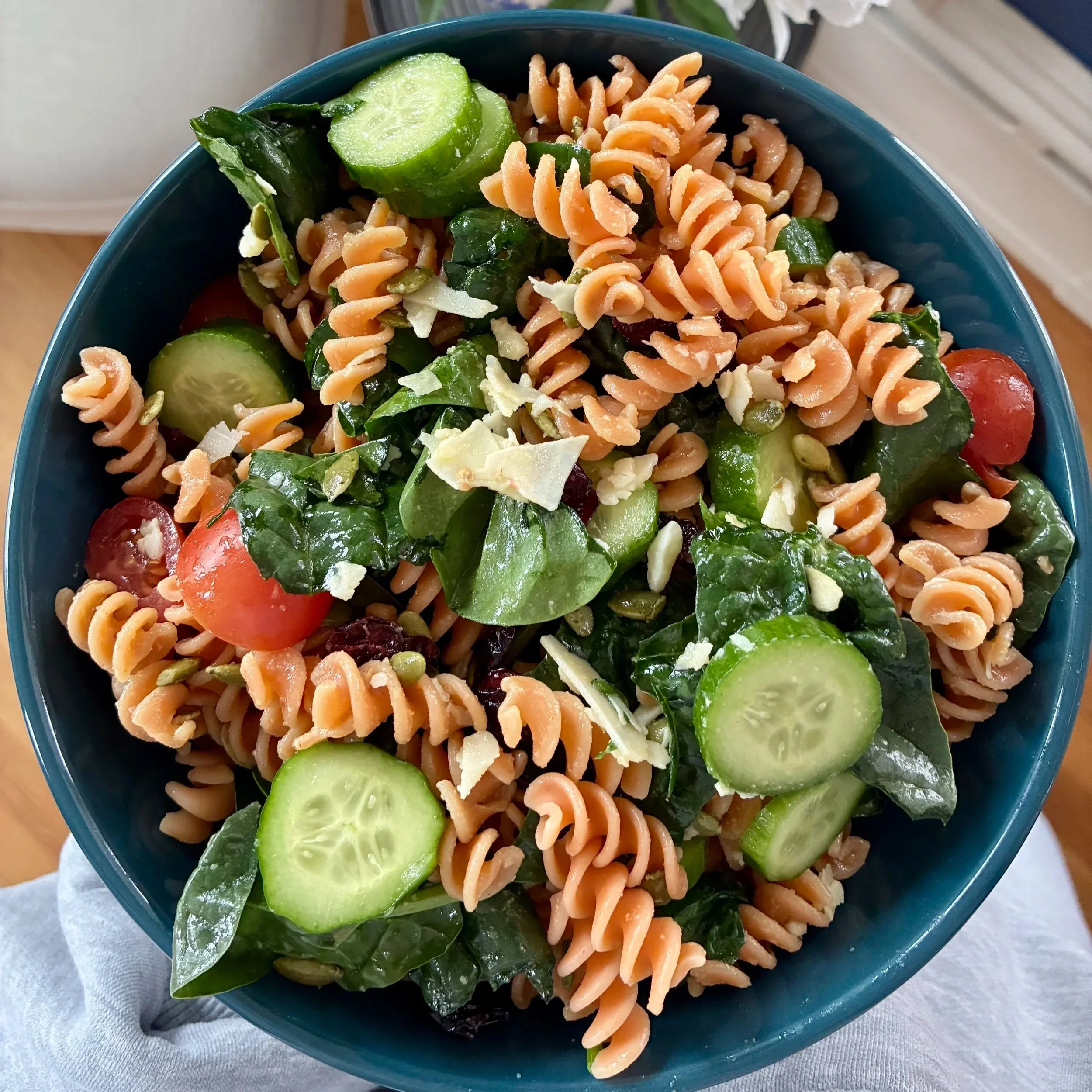 Bowl of pasta salad with rotini pasta, cherry tomatoes, cucumber slices, spinach, and shaved cheese