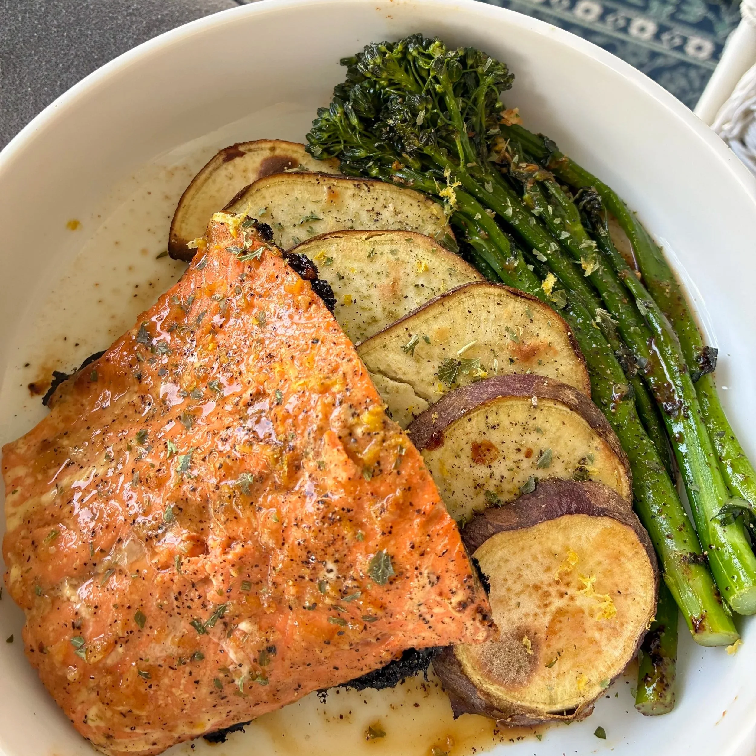 Baked salmon with seasoning, served with roasted zucchini slices and sautéed broccolini on a white plate.