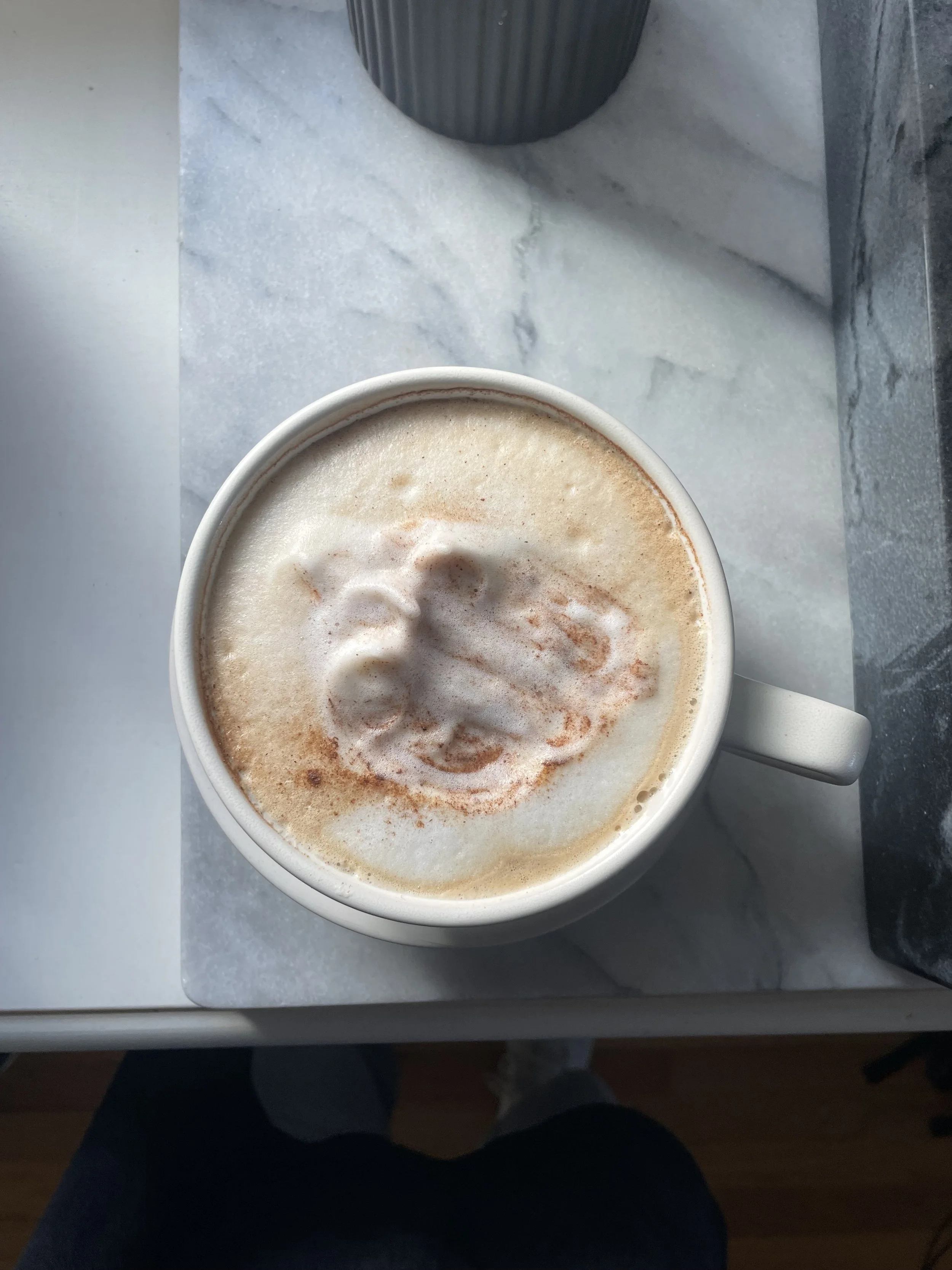 A cup of frothy coffee with latte art on top, placed on a marble countertop.