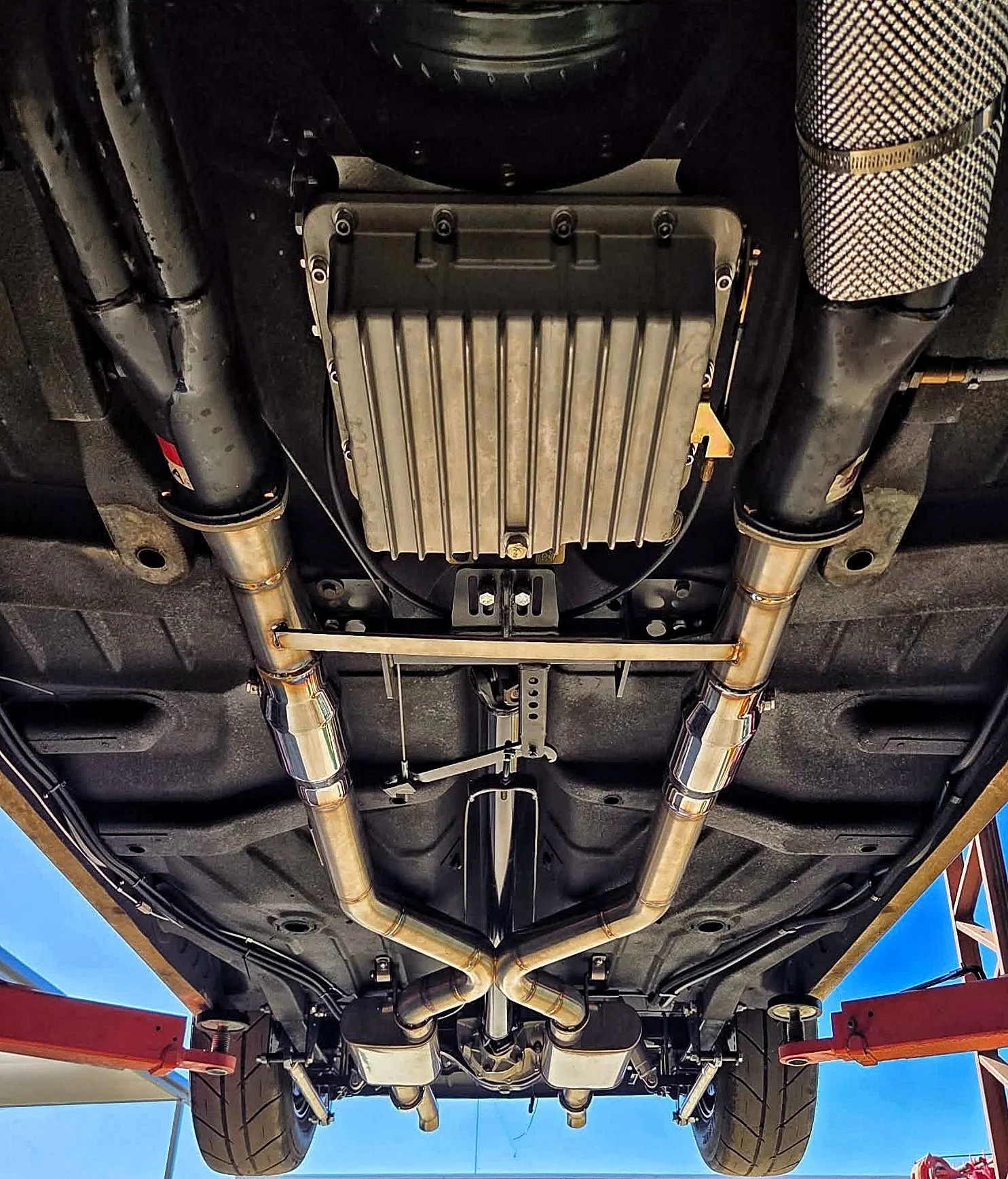 View of the underside of a racing car showing the exhaust system, differential, and other mechanical components.