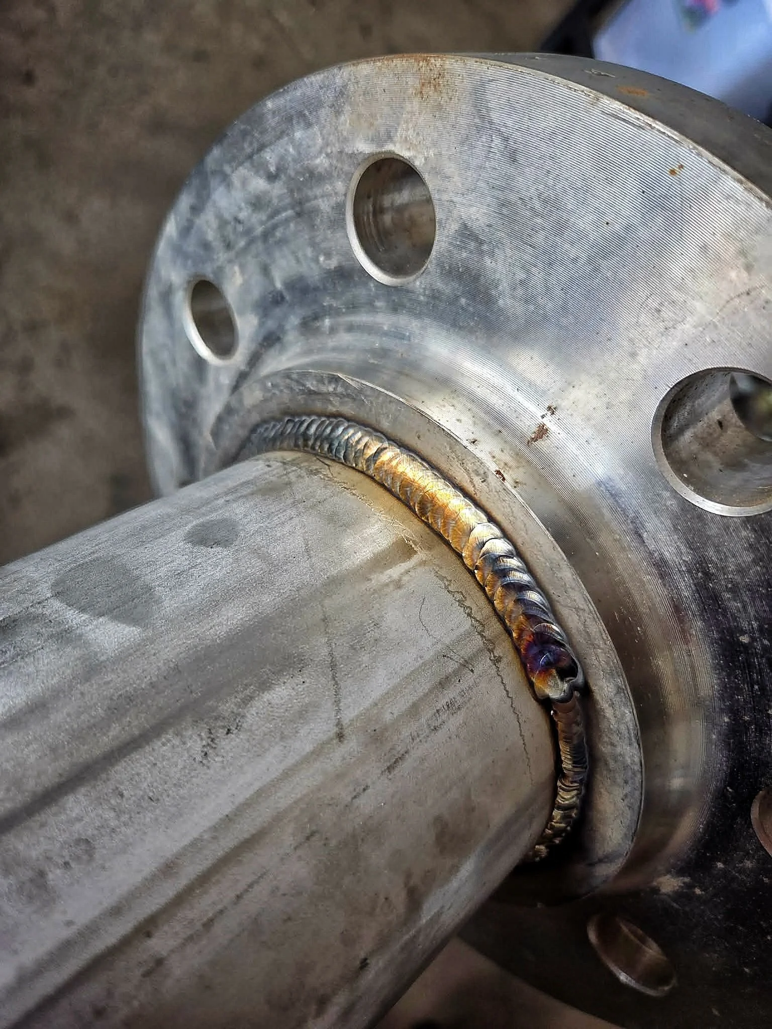 Close-up of a metallic mechanical component with welds and drilled holes.
