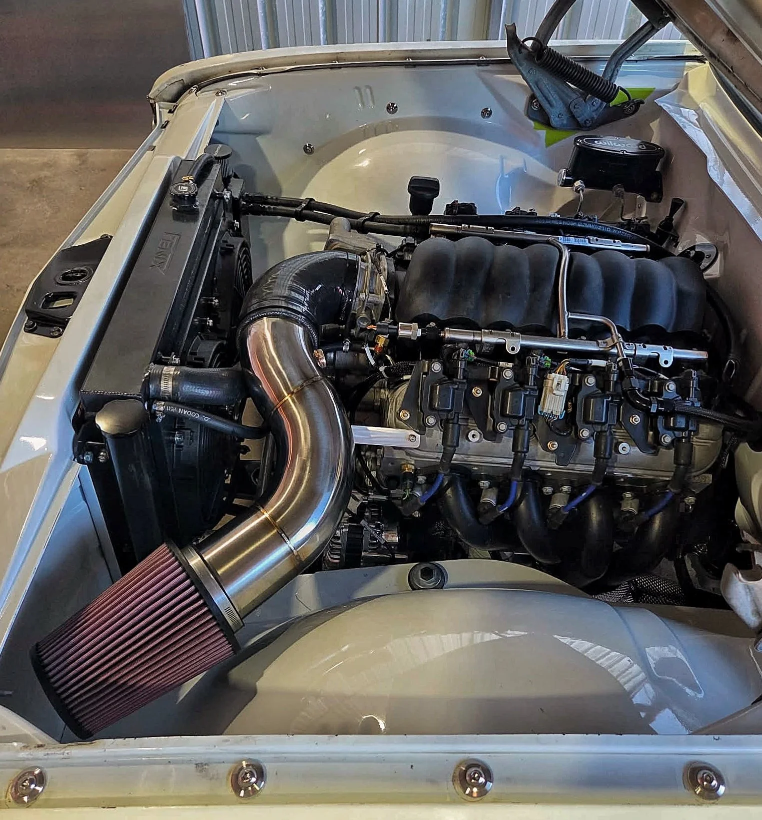 Close-up of a car engine inside the engine bay, featuring a turbocharger, red air filter, hoses, and other engine components.