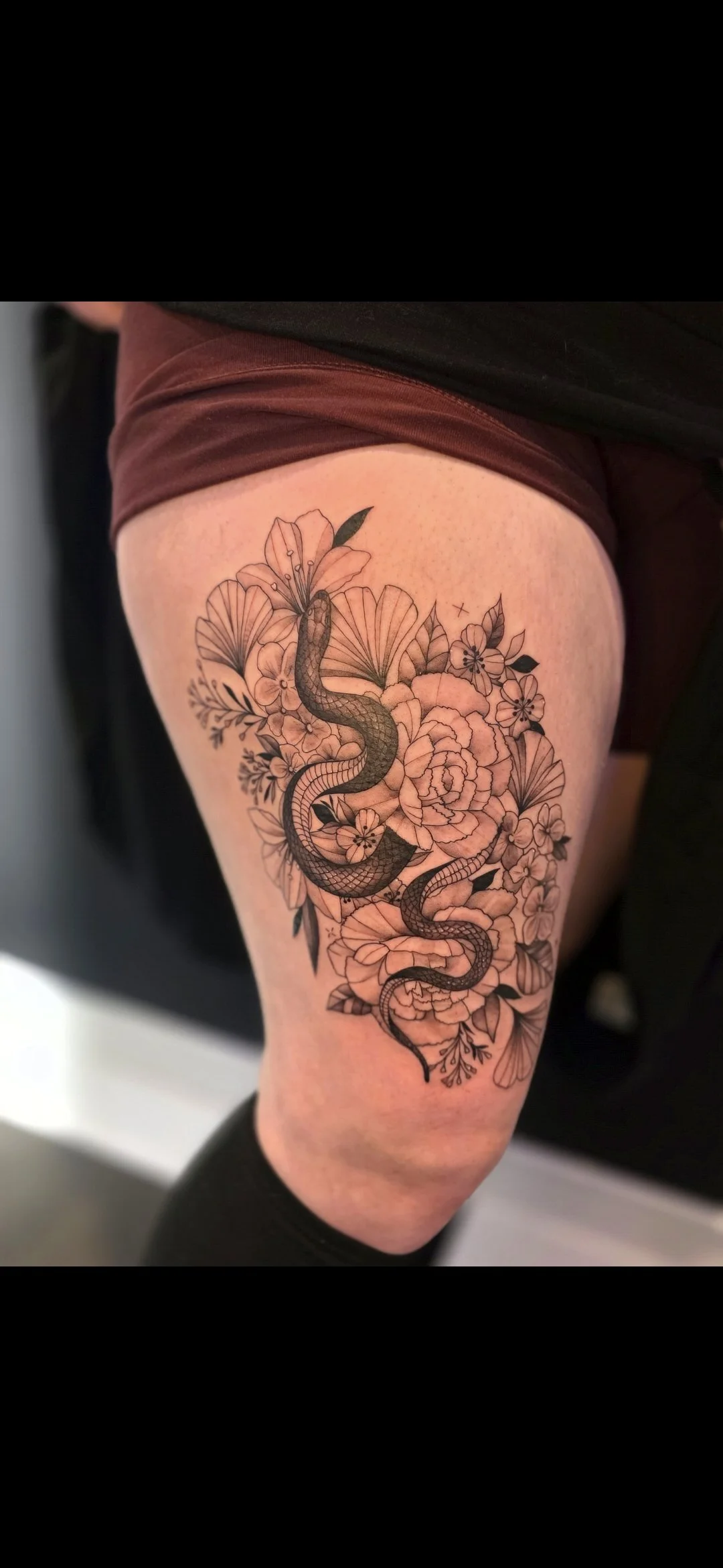 Tattoo of a snake intertwined with flowers on a person's thigh.