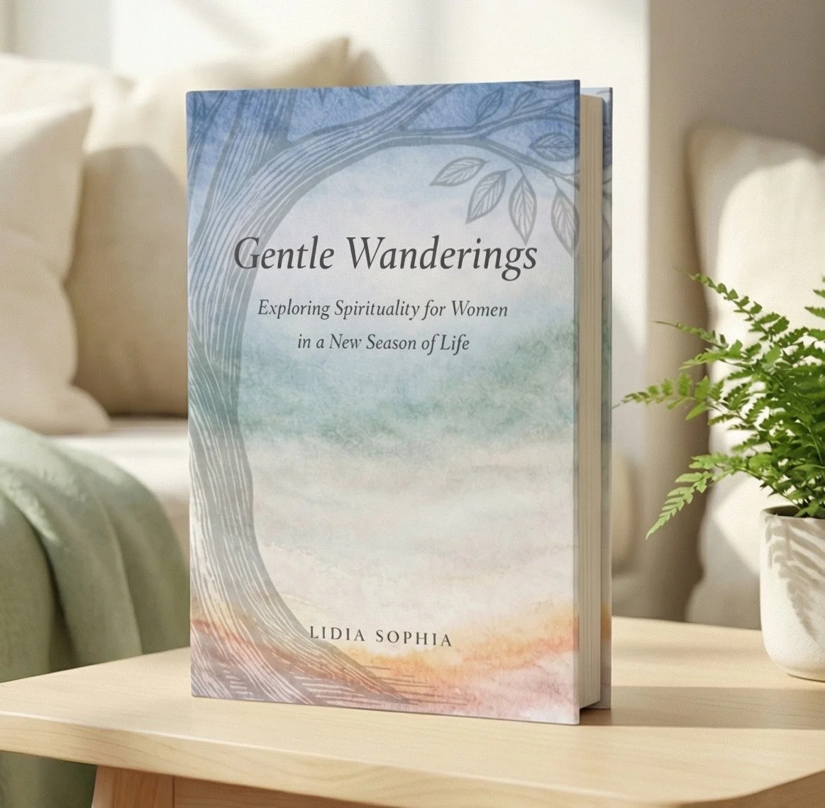A book titled "Gentle Wanderings" by Lidia Sophia standing upright on a light-colored table, with a green potted fern beside it. The book cover features a soft watercolor design with tree branches and leaves, and the subtitle "Exploring Spirituality for Women in a New Season of Life." The background shows a cozy room with a bed and cushions.