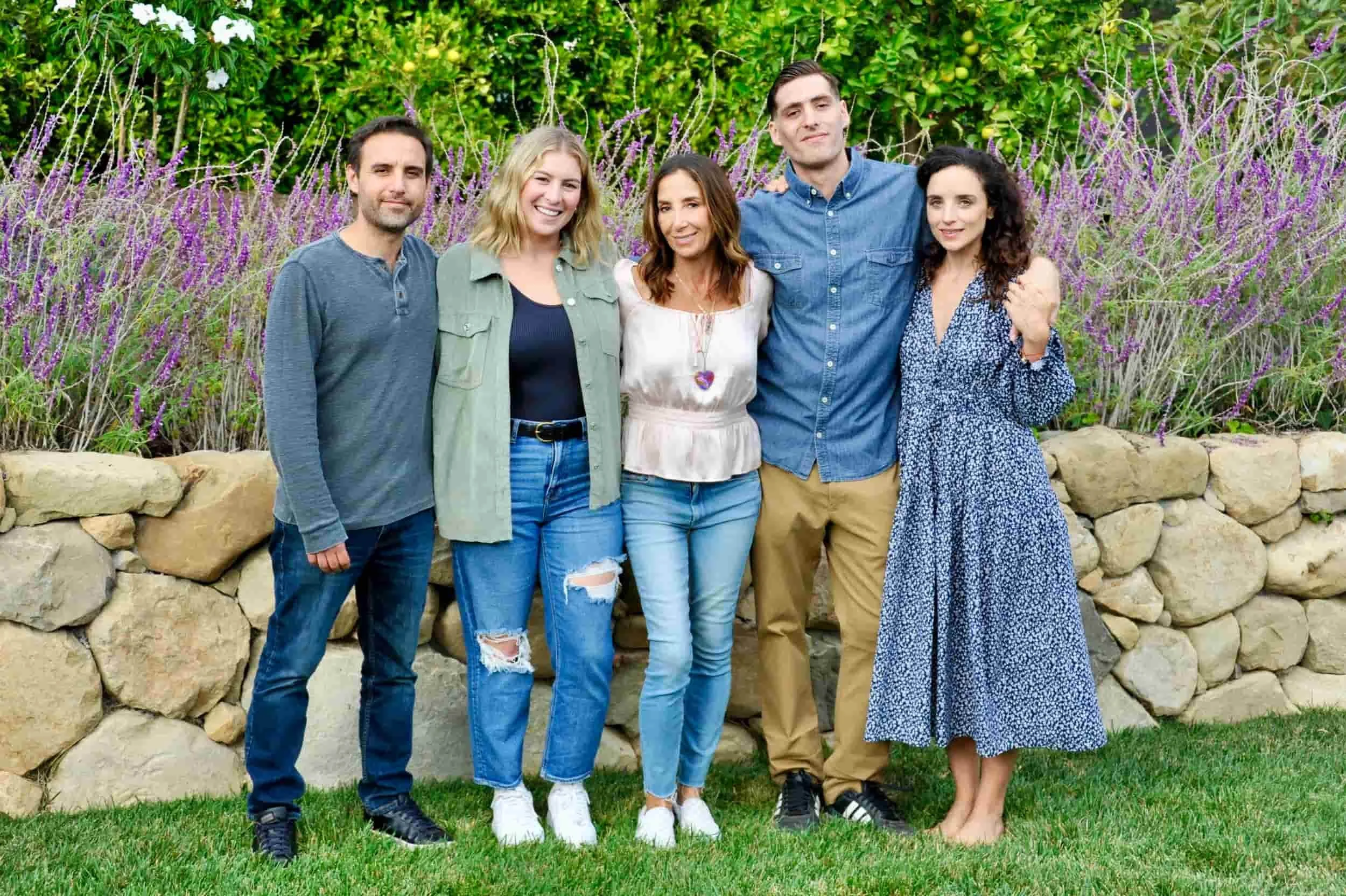 Group of five people standing outdoors in front of purple flowers and green foliage, smiling at the camera.