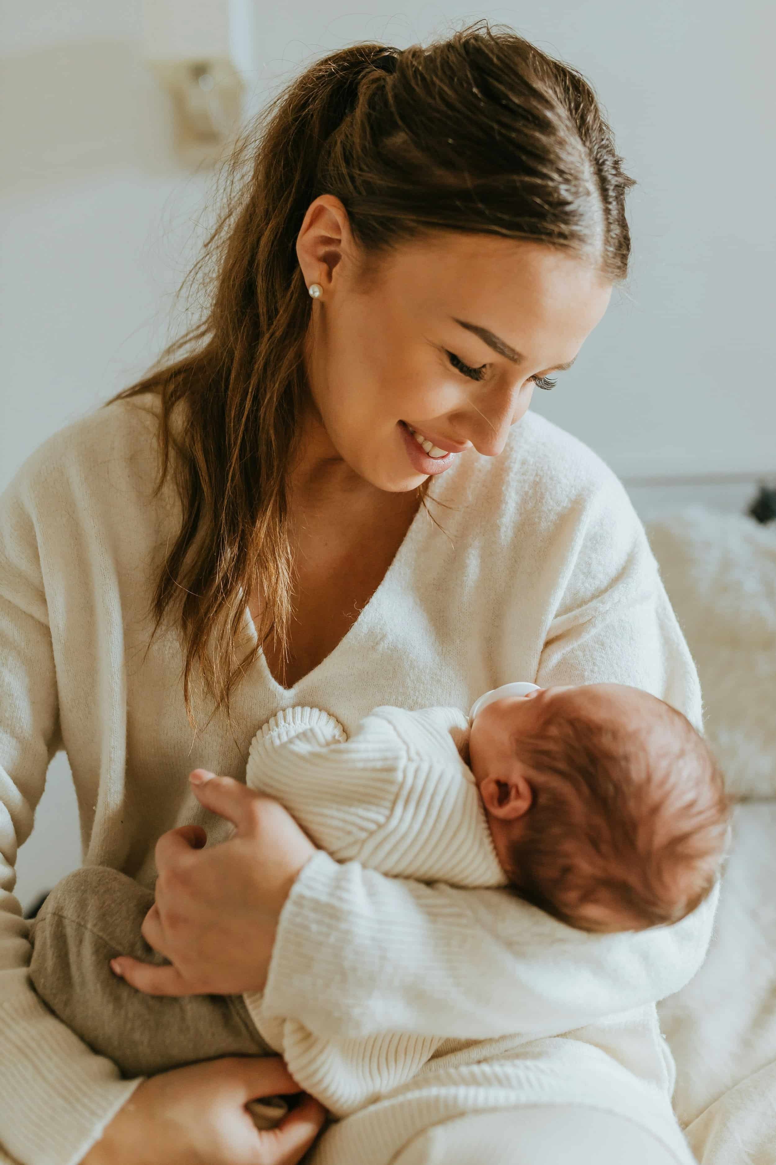 Caring doula warmly cradling newborn baby indoors, Om Baby doula placement services Los Angeles