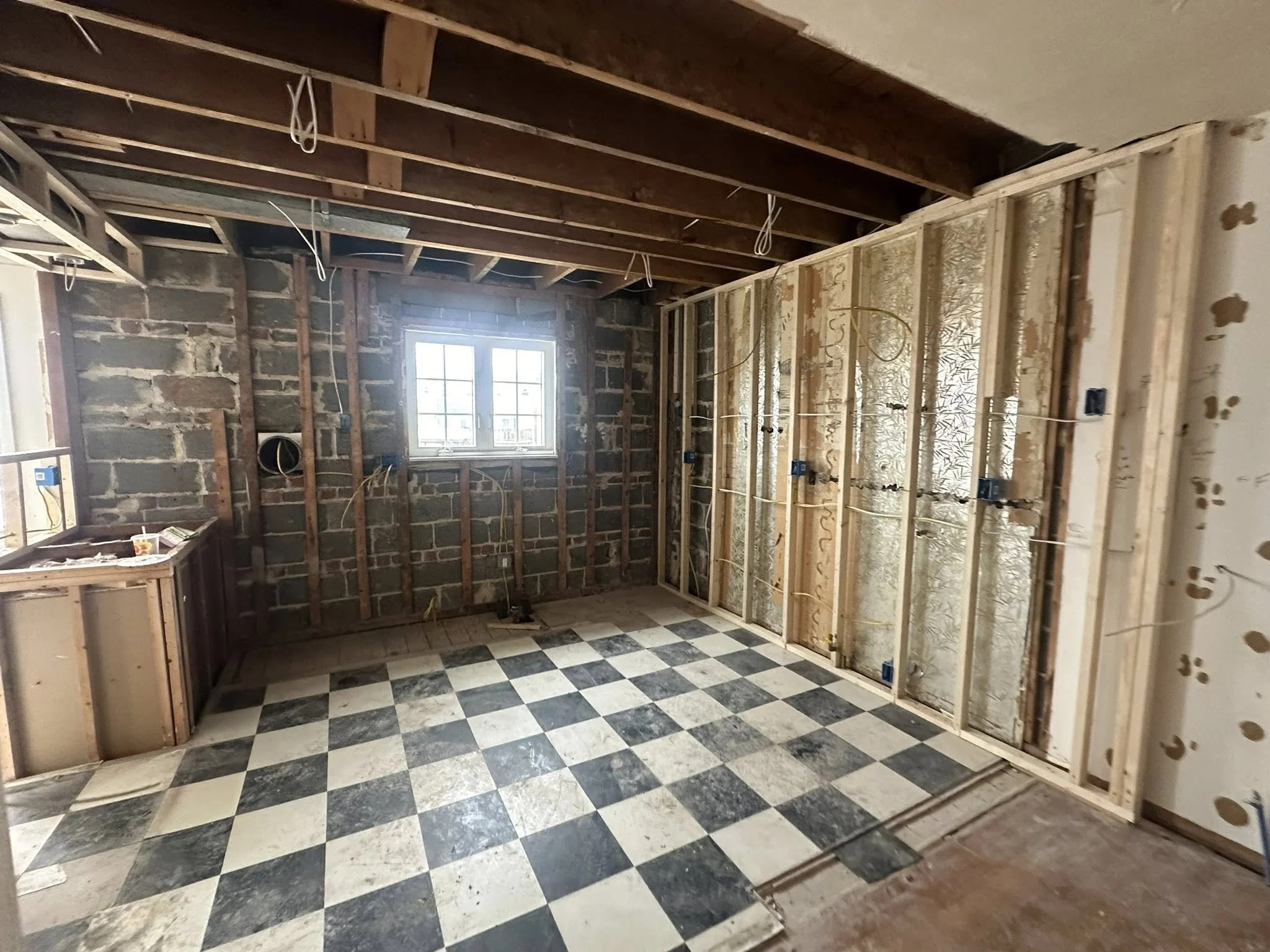 Interior of a room under renovation with exposed ceiling beams, unfinished walls, and checkered black and white floor tiles.