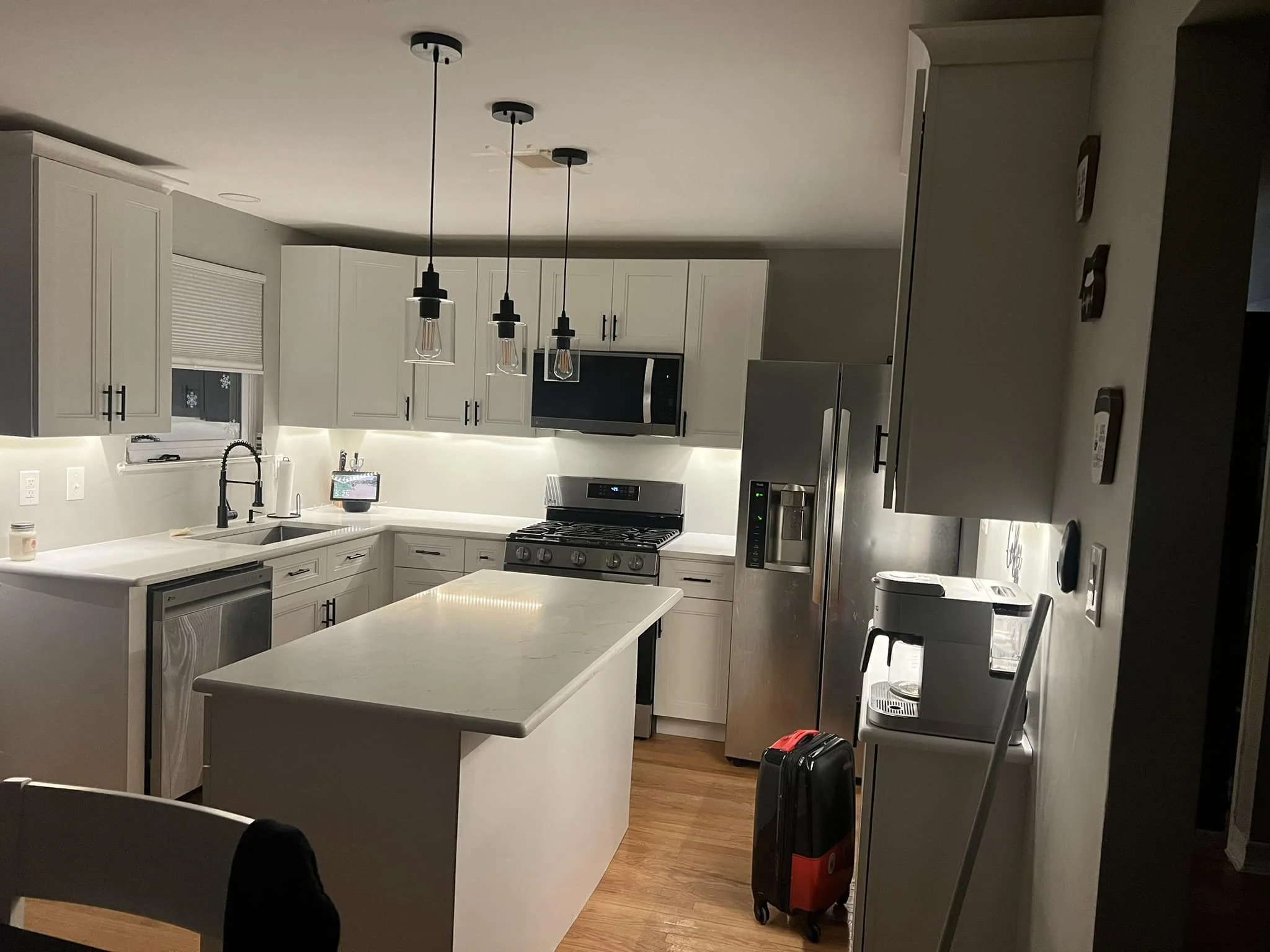 Modern kitchen with white cabinets, black hardware, stainless steel refrigerator and stove, white countertop island, and pendant lighting.
