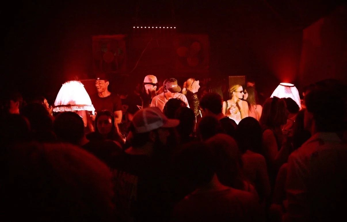 A crowded indoor music venue with a stage, featuring several performers and audience members in low lighting.