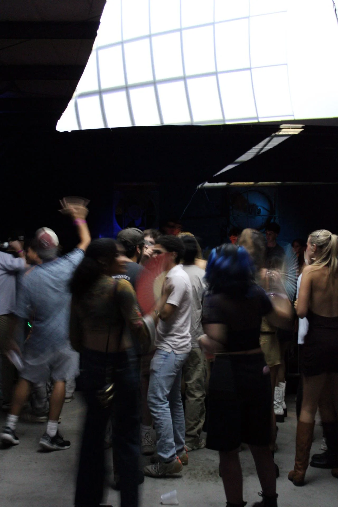 People dancing and socializing at a dark indoor party with a brightly lit ceiling.