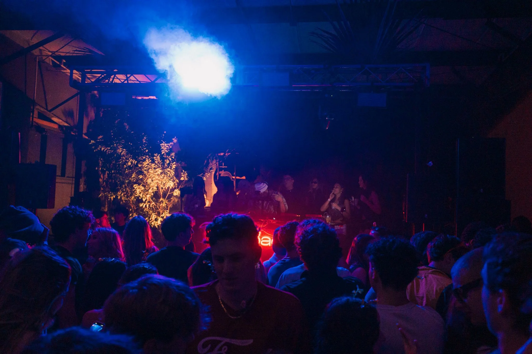 A crowded indoor party or club with people dancing and socializing, illuminated by blue and pink stage lighting.