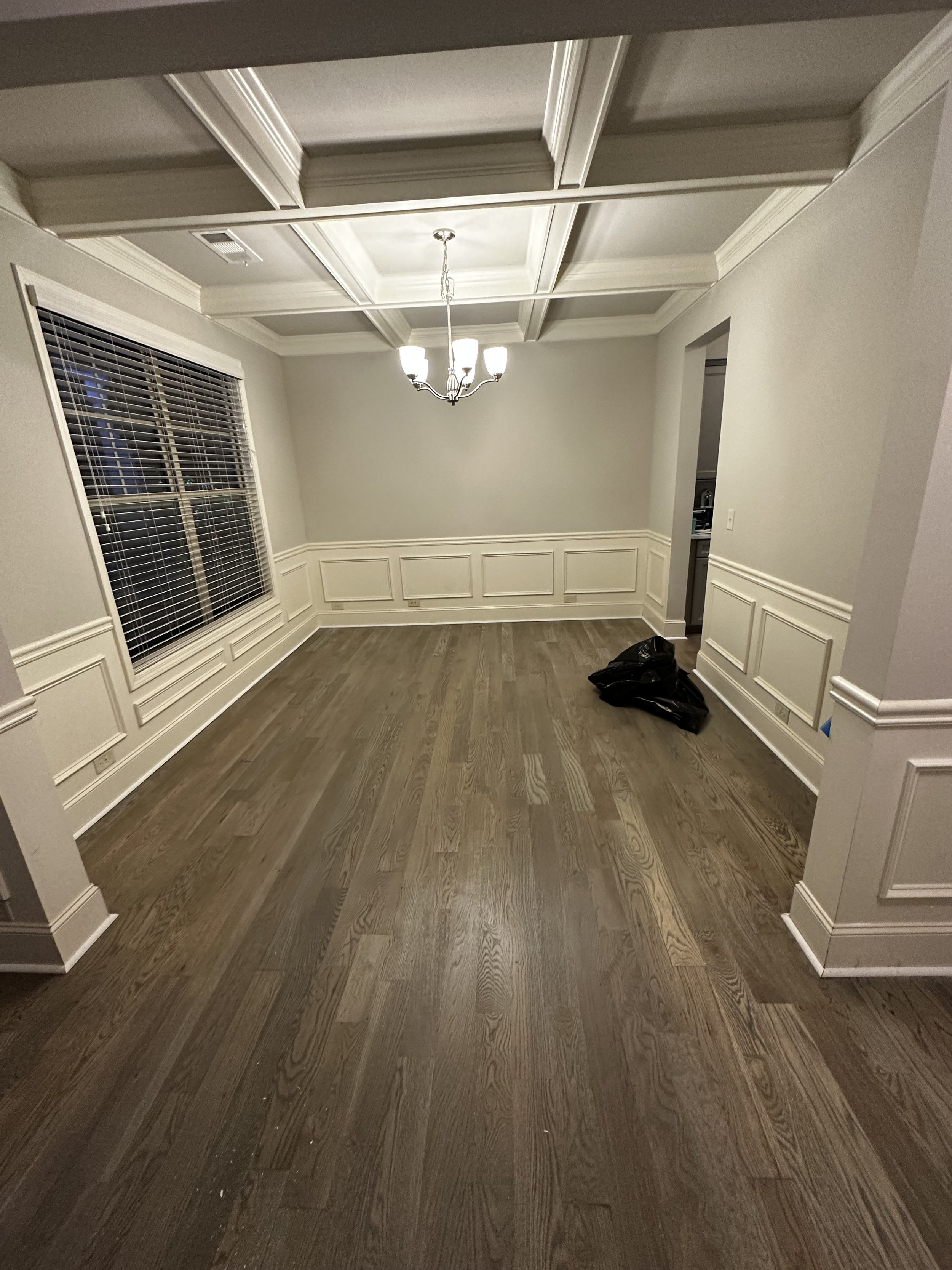 Empty dining room with hardwood floors, white wainscoting and crown molding, a window with blinds, and a chandelier pendant lighting.