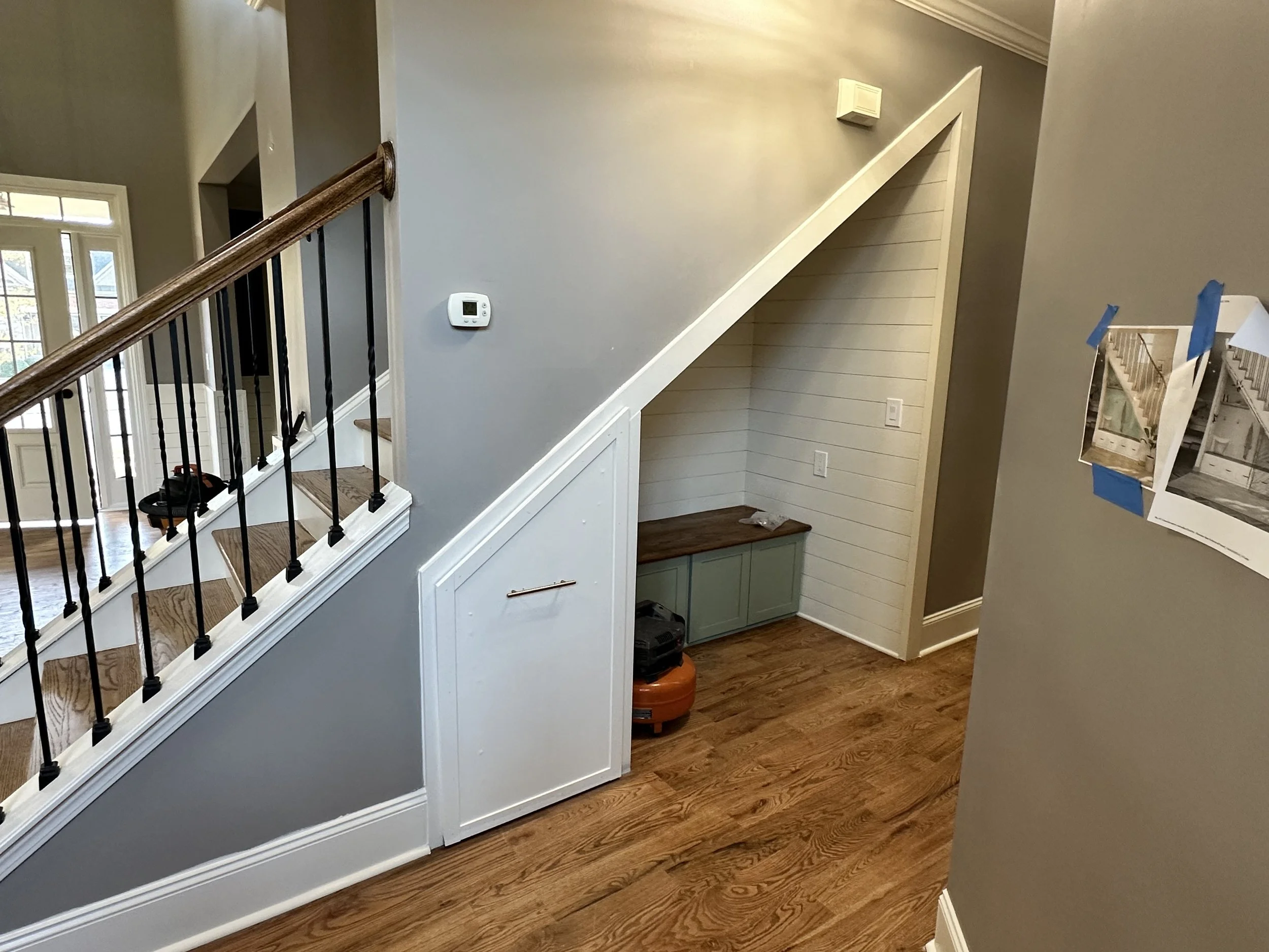Interior view of a house with stairs, a small built-in cabinet, and wall pictures taped to the wall.