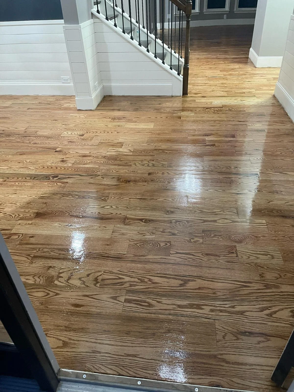 Shiny wooden flooring in an entryway with stairs and walls painted in light gray and white.