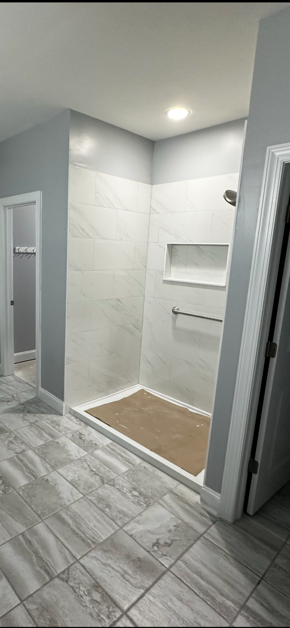 Empty shower stall with white marble tiles, built-in niche, towel bar, and a brown mat on the floor, with a ceiling light overhead.