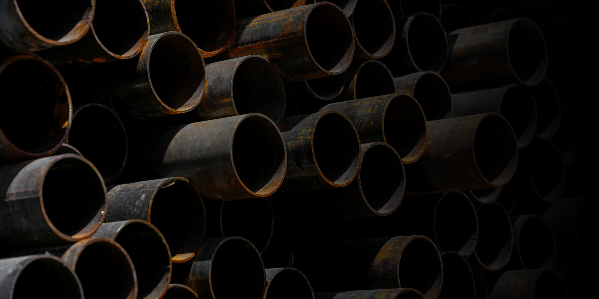 Stacks of rusty metal pipes arranged horizontally in a storage area.