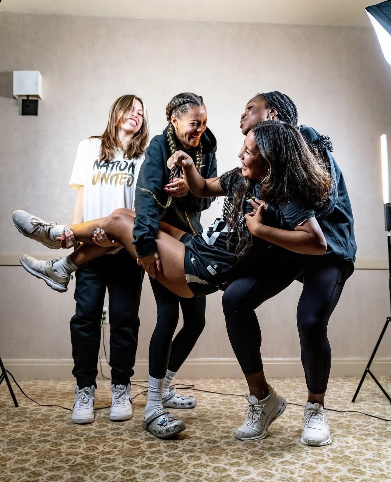 Group of four women celebrating with one woman being lifted in the air, smiling and laughing.