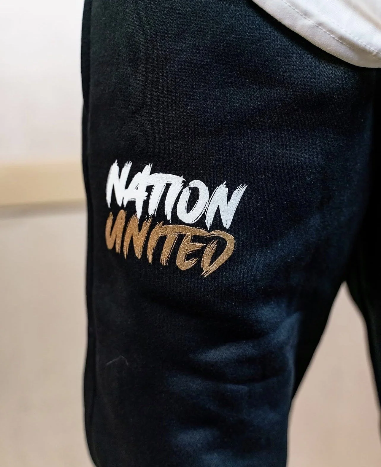 Close-up of black pants with the words 'NATION WINTERD' embroidered in white and brown on the thigh.