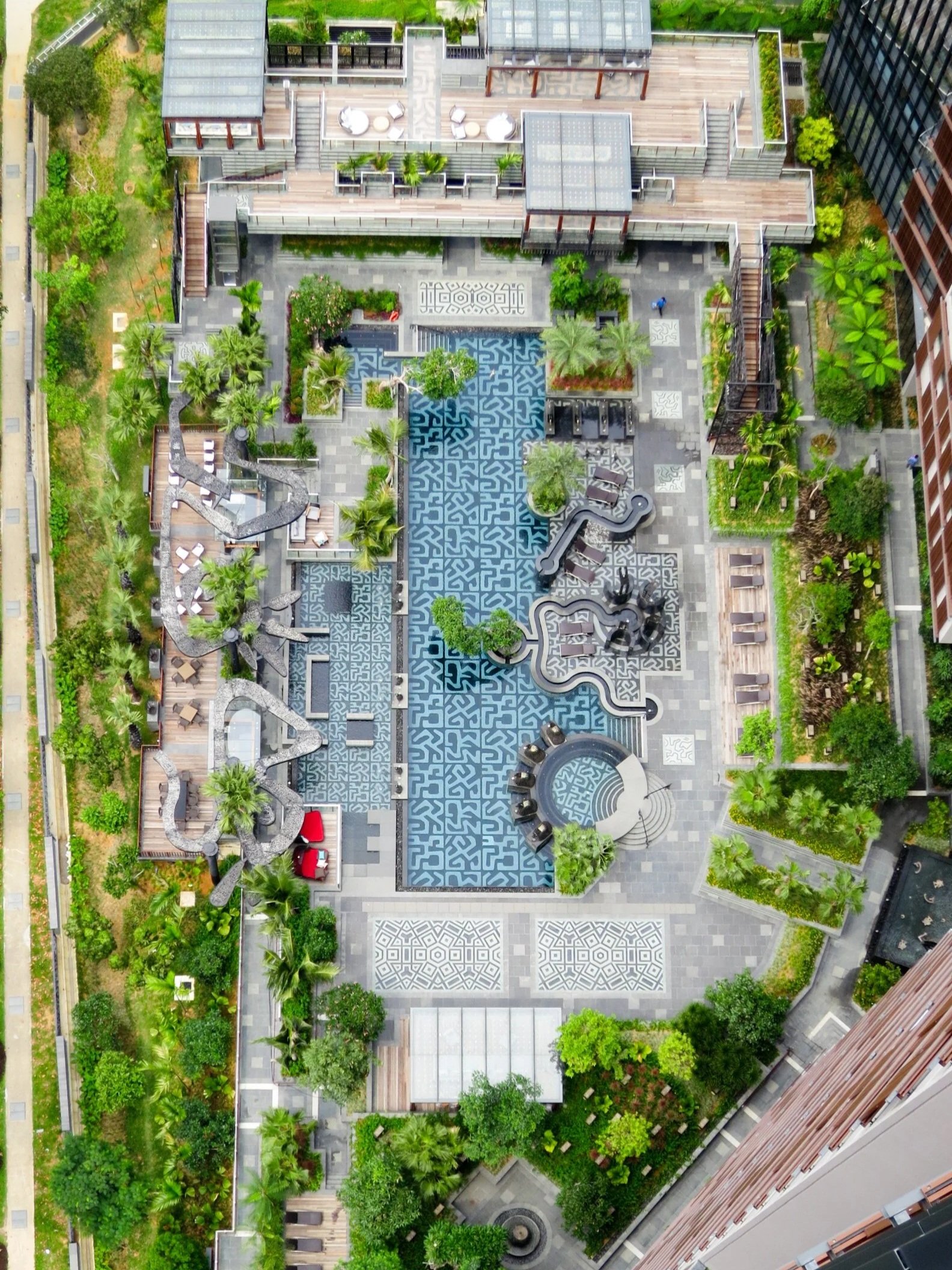 Aerial view of a modern rooftop garden and recreational area with trees, plants, pathways, seating, and decorative surfaces in an urban setting.