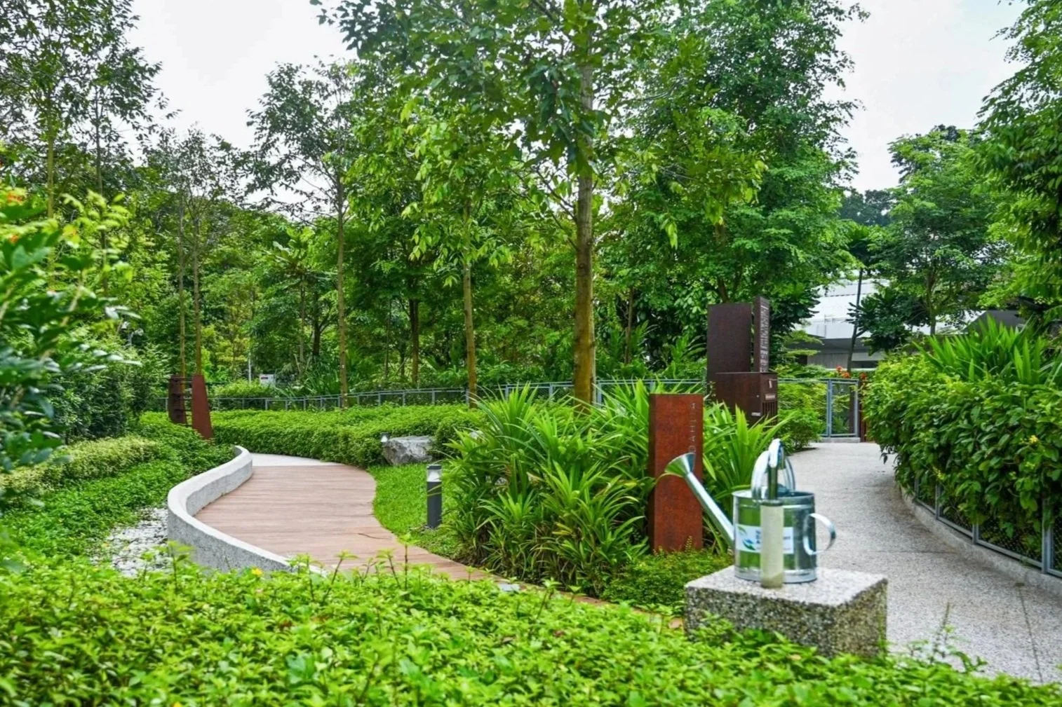 A lush green park with a winding pathway, trees, shrubs, and decorative metal sculptures.