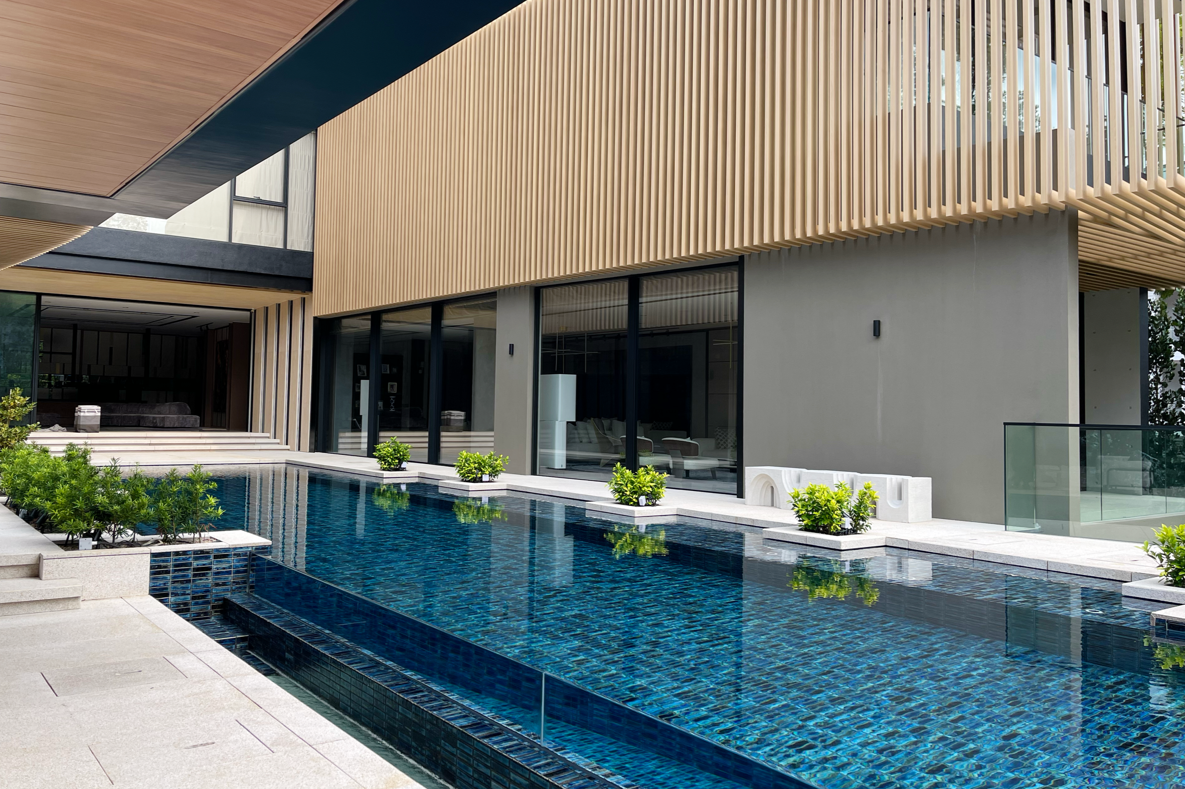 Modern house with large glass windows, wooden and concrete exterior, side view with swimming pool and plants in the foreground.