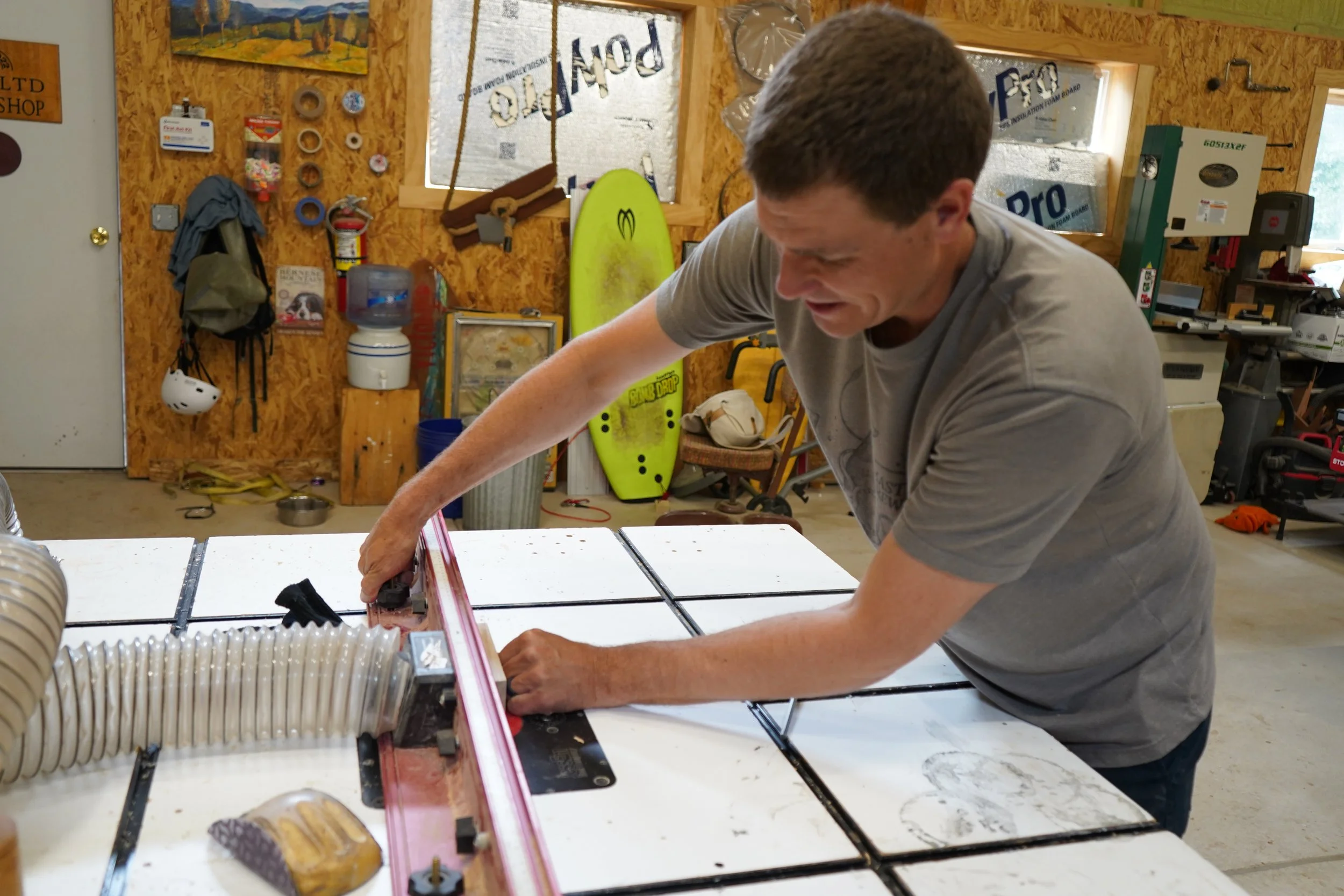 A man working in a woodworking or construction workshop, using a saw or cutting tool on a worktable.
