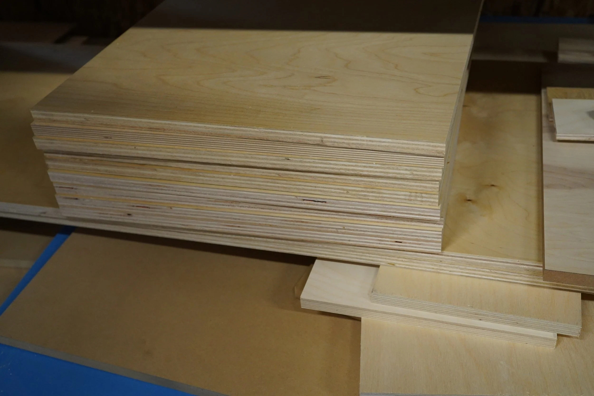 Stack of plywood sheets on a workbench in a woodworking shop.