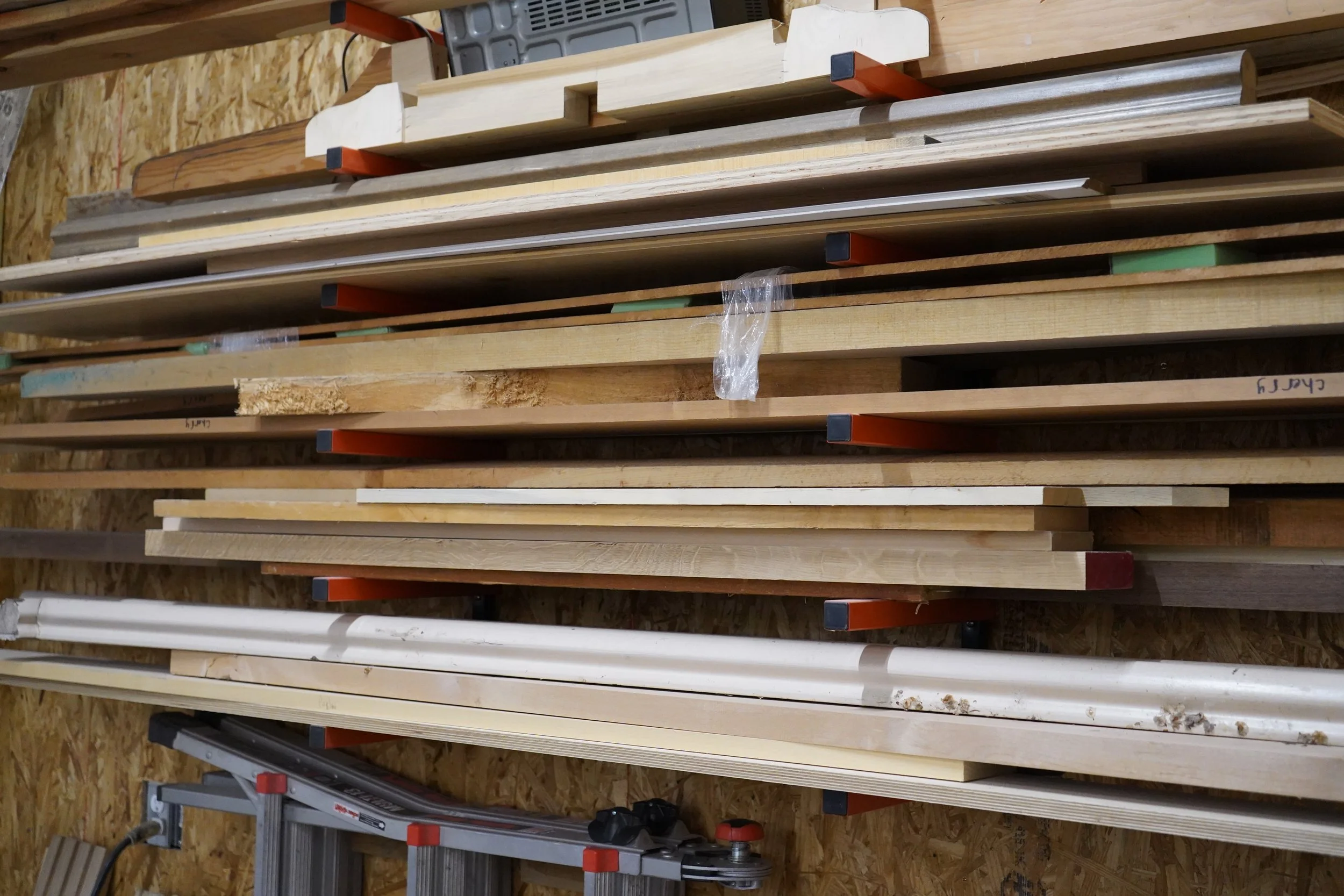 Multiple wooden planks and pieces stored on a wall-mounted rack in a woodworking shop.
