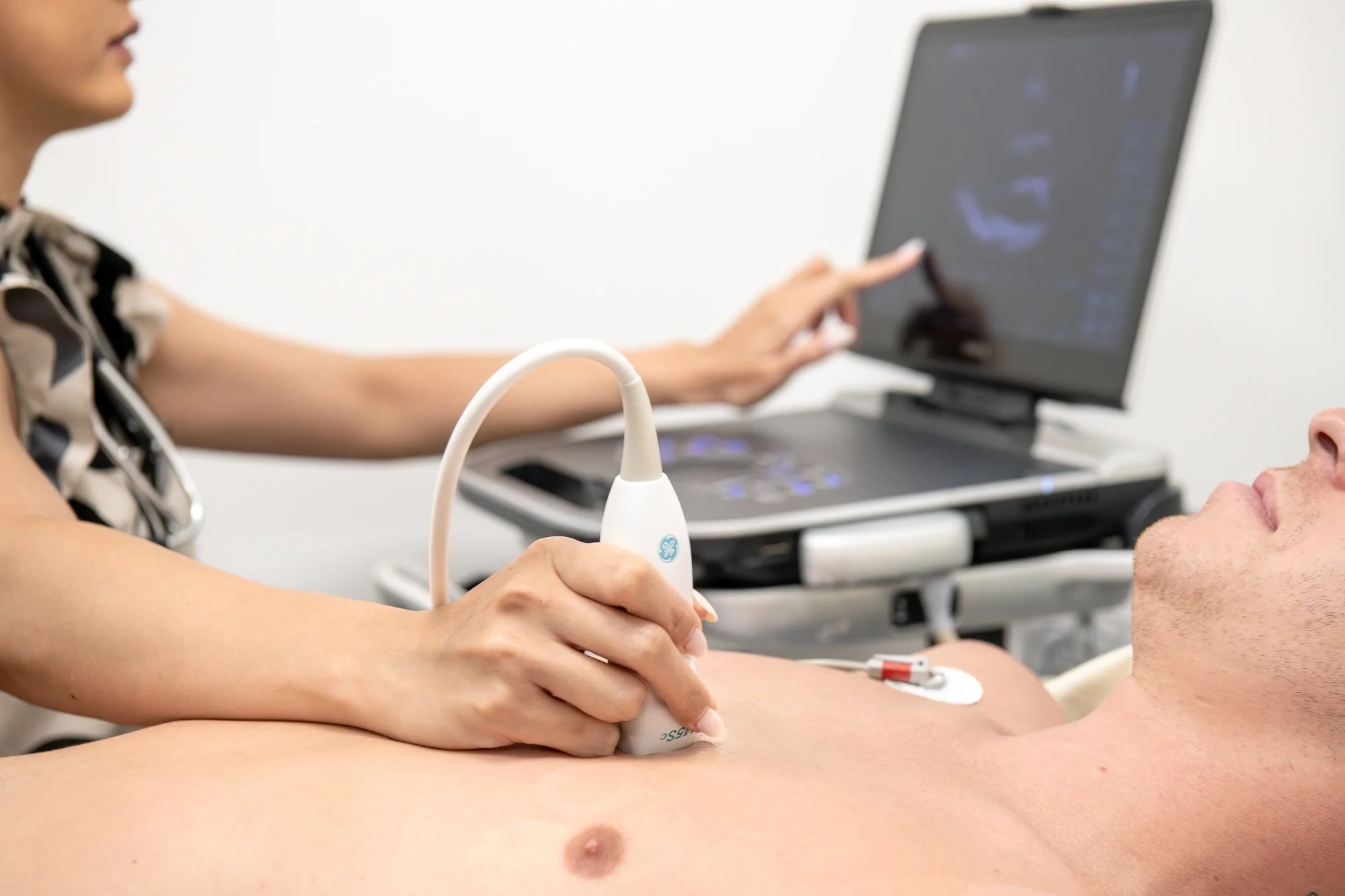 A medical professional performs an ultrasound exam on a patient's abdomen using an ultrasound probe connected to a laptop with an ultrasound image displayed on the screen.