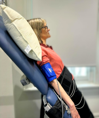 A woman in a hospital bed with a blood pressure cuff on her arm, sitting upright and looking to the side.