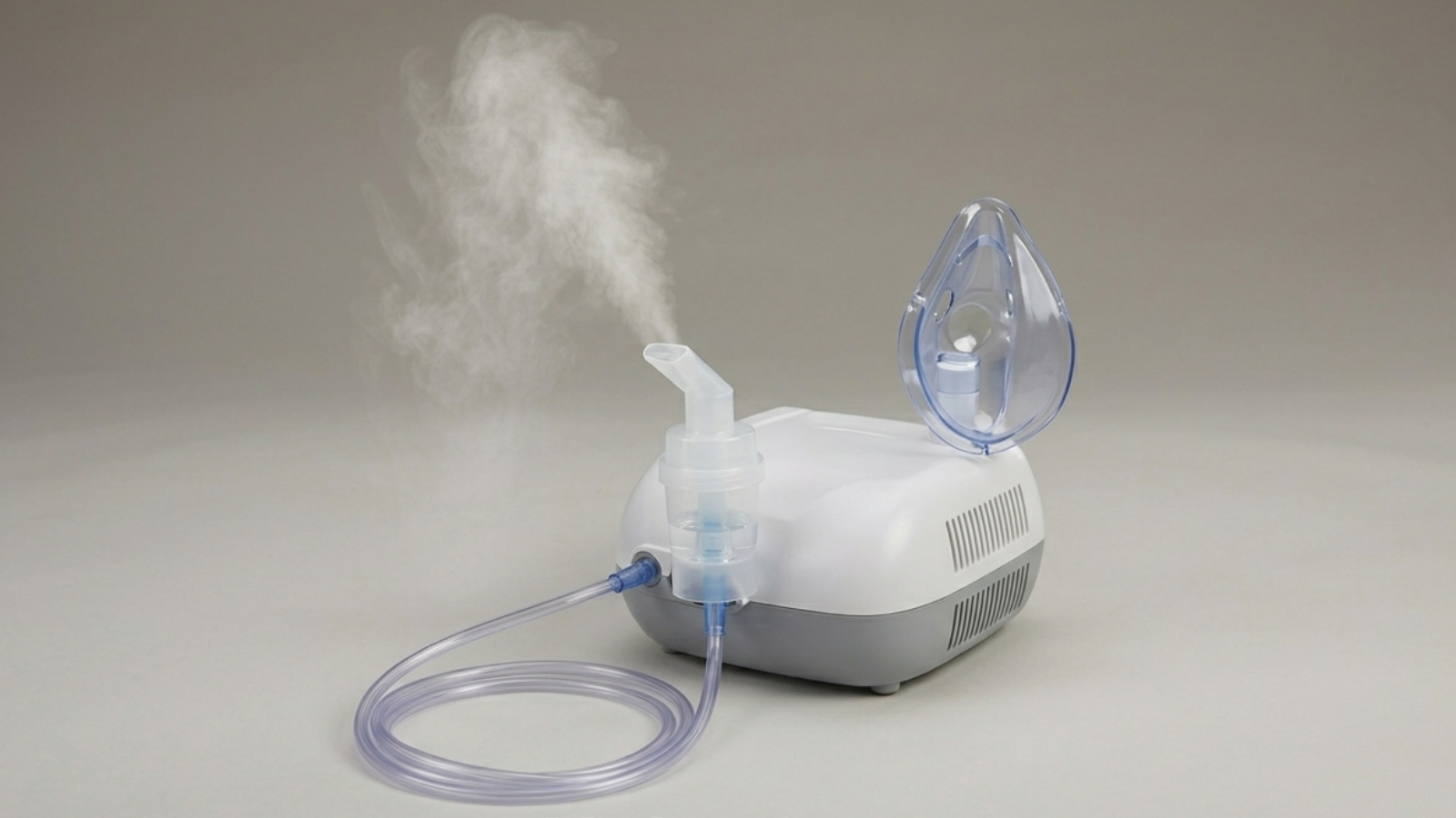 A small medical nebulizer with a clear face mask, tubing, and mist coming out of the mouthpiece, set against a plain background.
