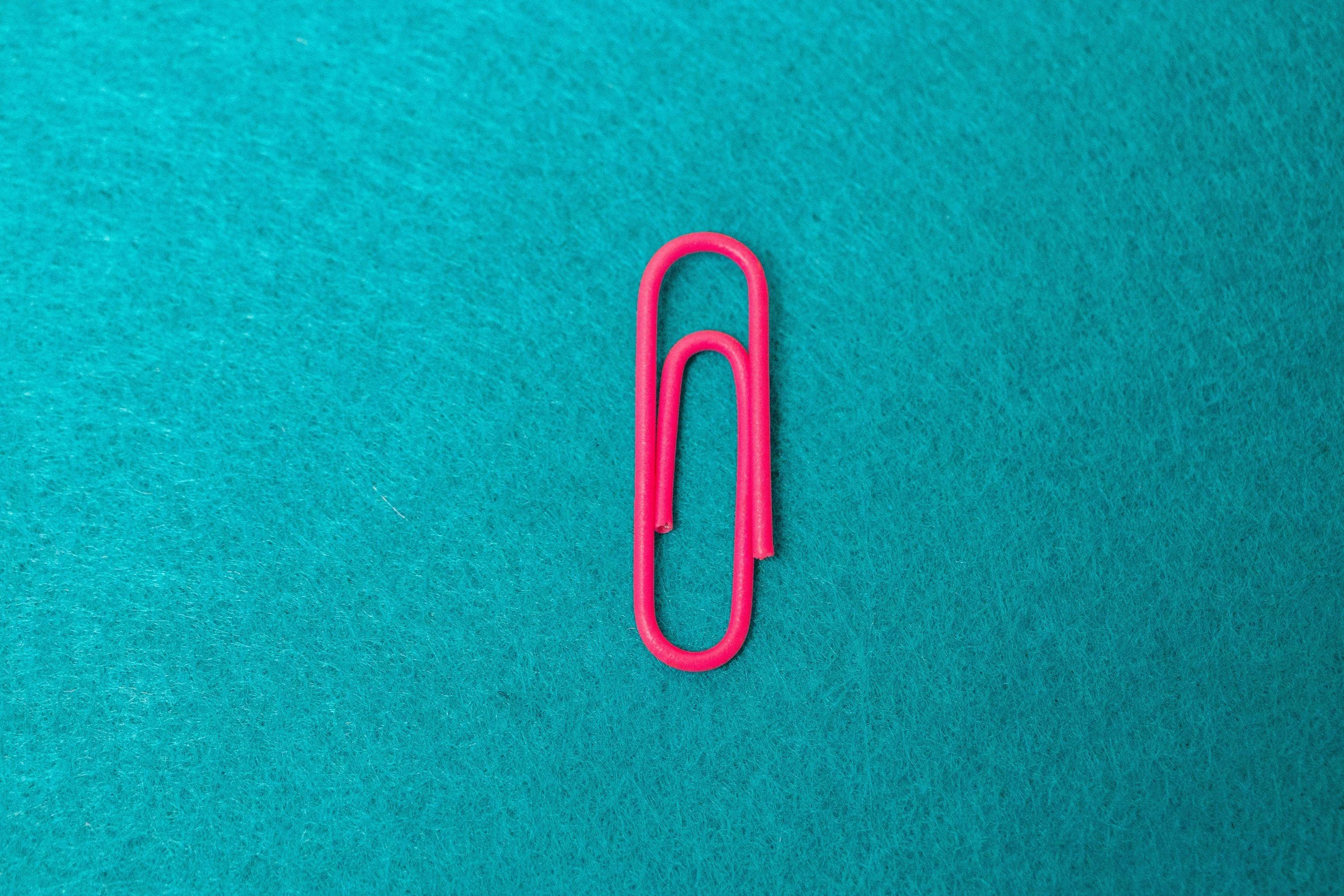 A pink paperclip on a teal textured background.