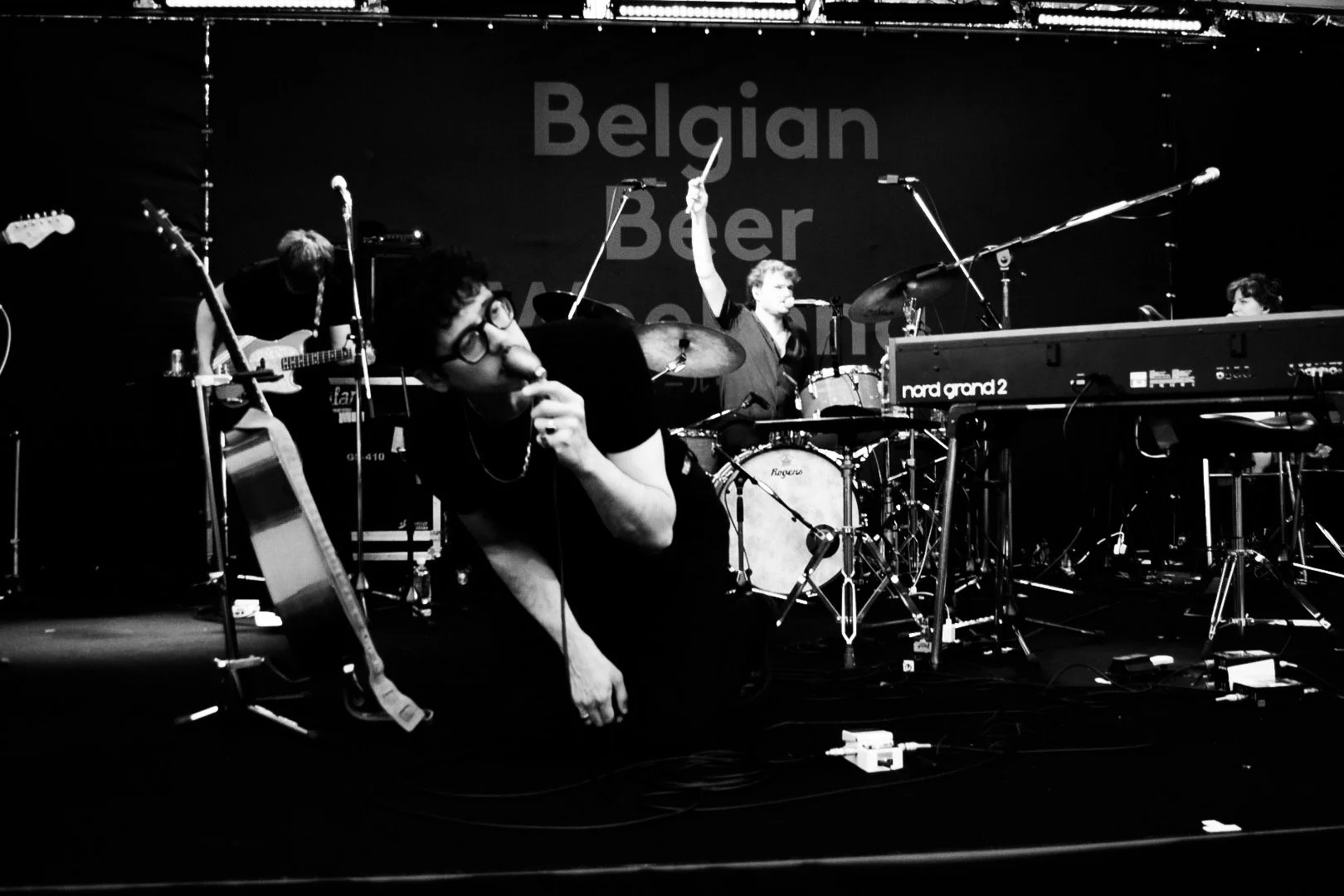 Fotografia em preto e branco da banda Dressed Like Boys durante apresentação ao vivo no Belgian Beer Weekend, em Nagoya, com vocalista, bateria e teclado no palco.