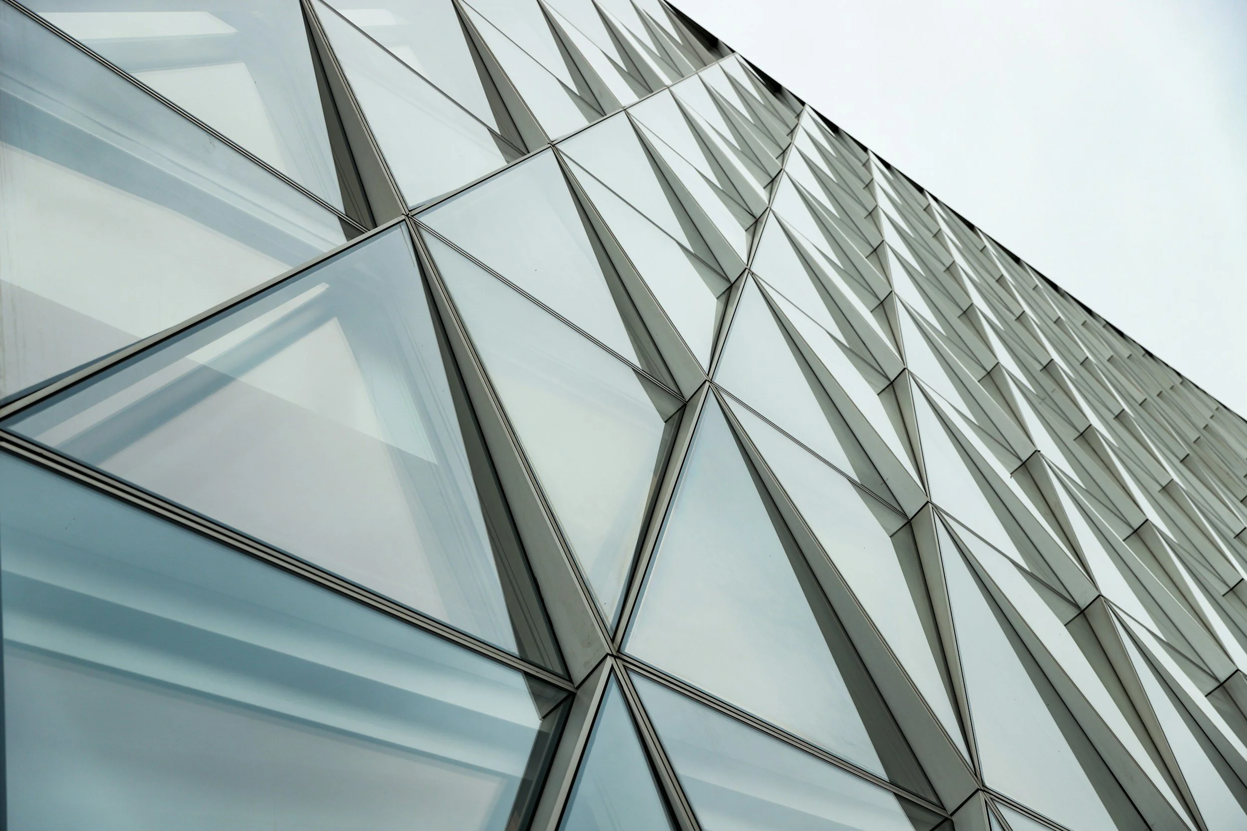 A modern building with a glass facade featuring geometric patterns, viewed from below against an overcast sky.