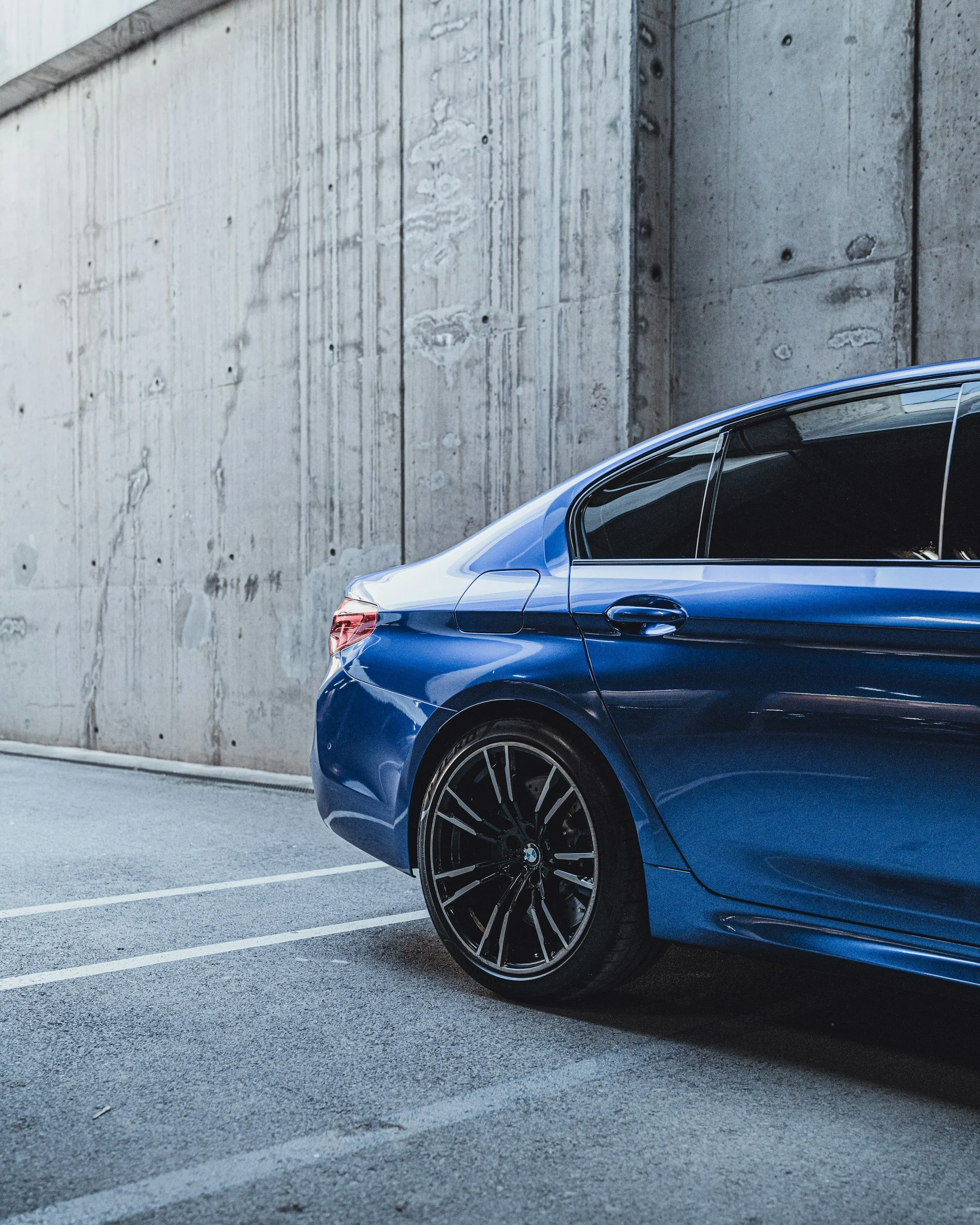 Close-up side view of a blue BMW car parked in a parking lot, with a concrete wall in the background.