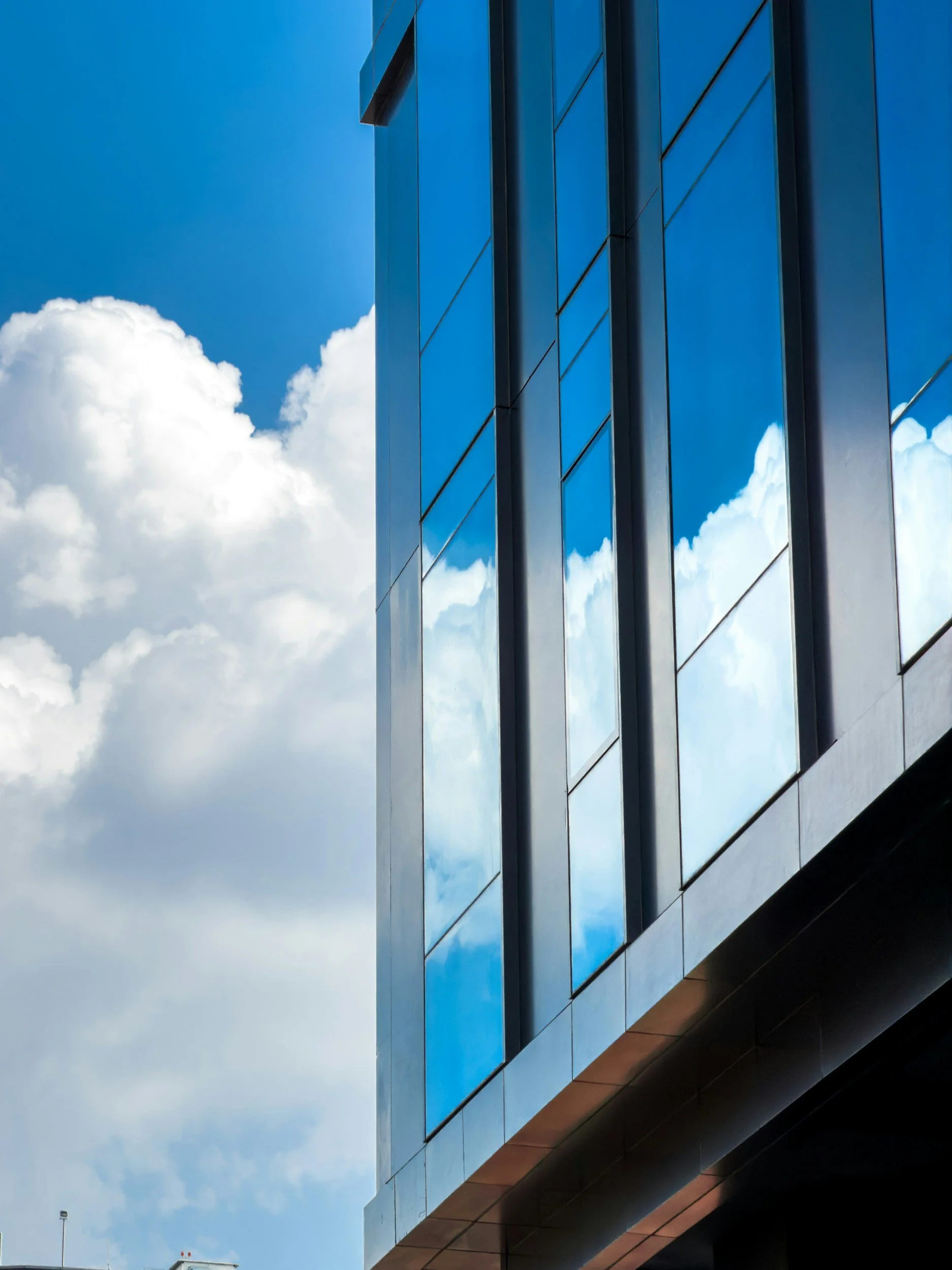 Modern building with reflective blue glass windows against a blue sky with clouds.