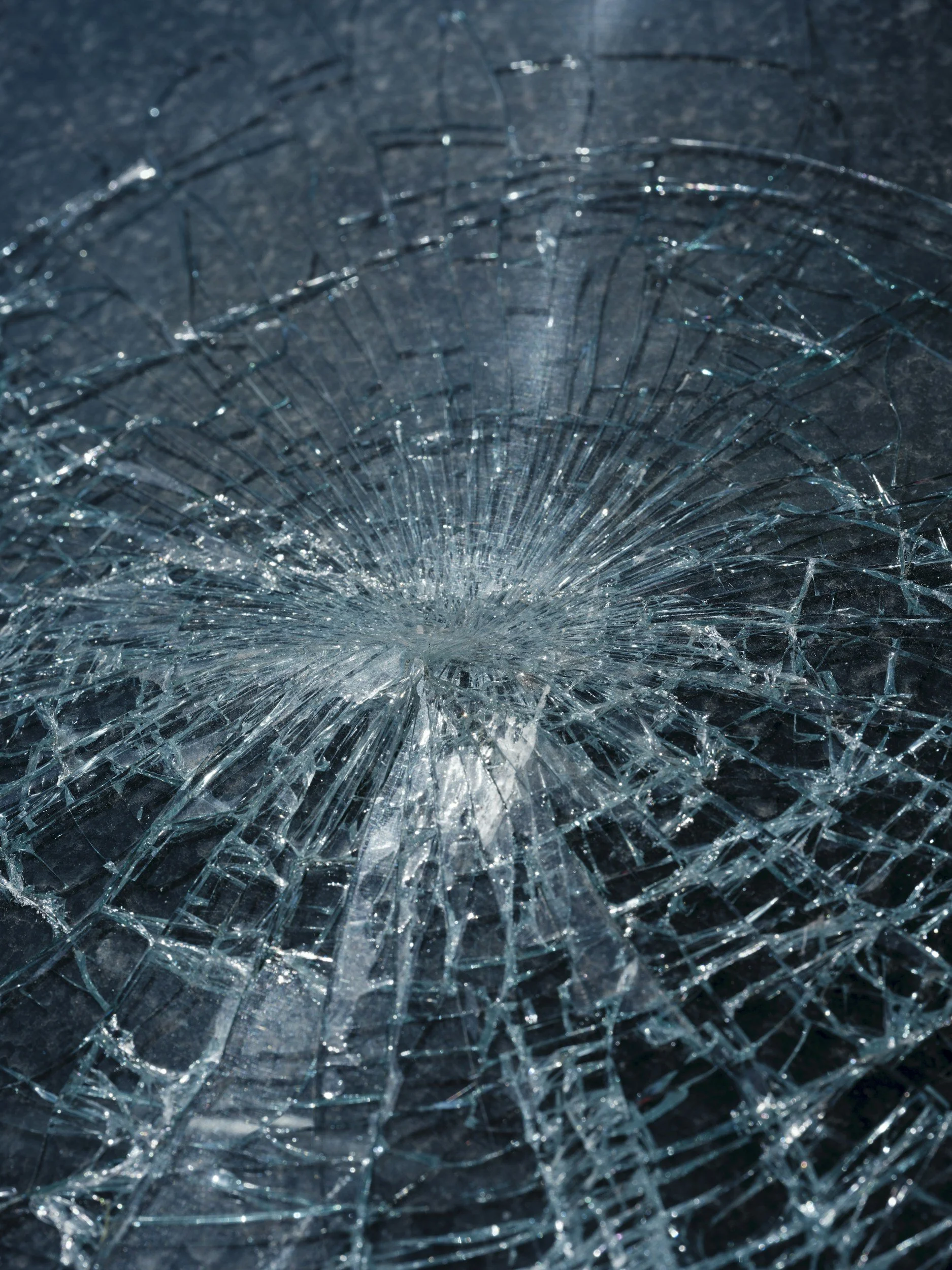 Close-up of shattered glass with numerous cracks radiating from the center.
