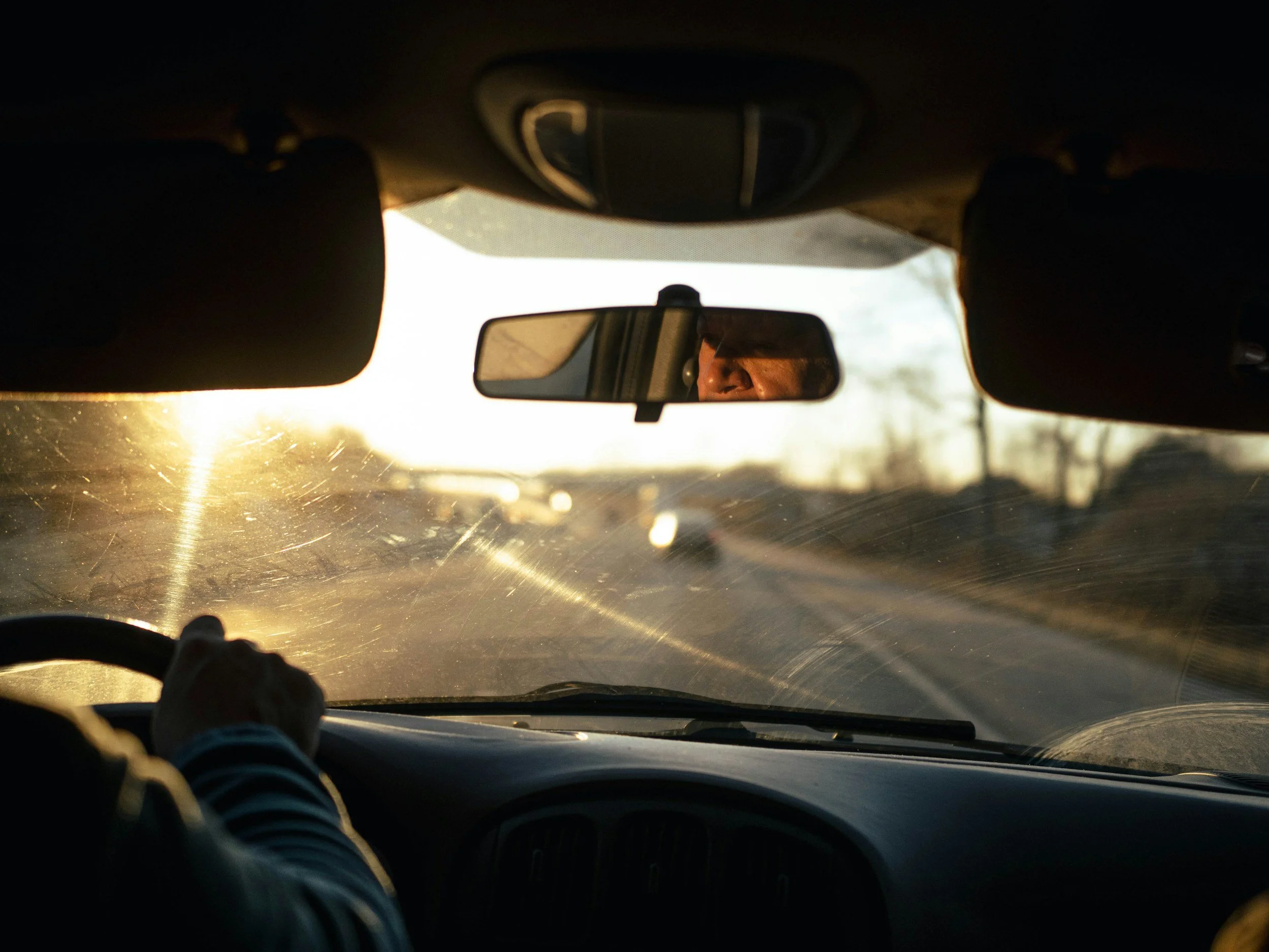View from inside a car looking at the rearview mirror and dashboard with sunlight shining through the windshield.