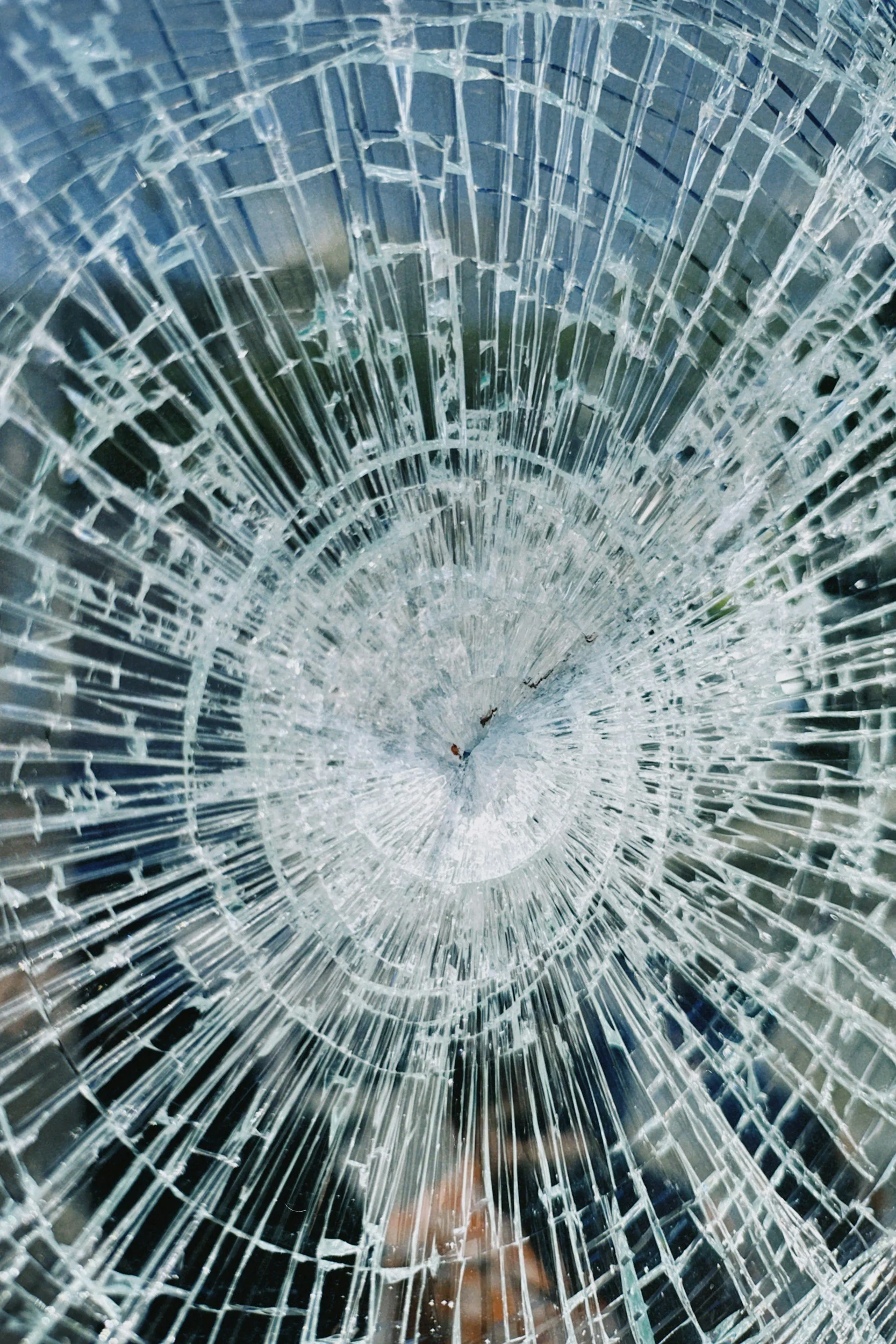 Close-up view of a shattered glass surface with multiple cracks radiating outward, creating a spiderweb pattern.