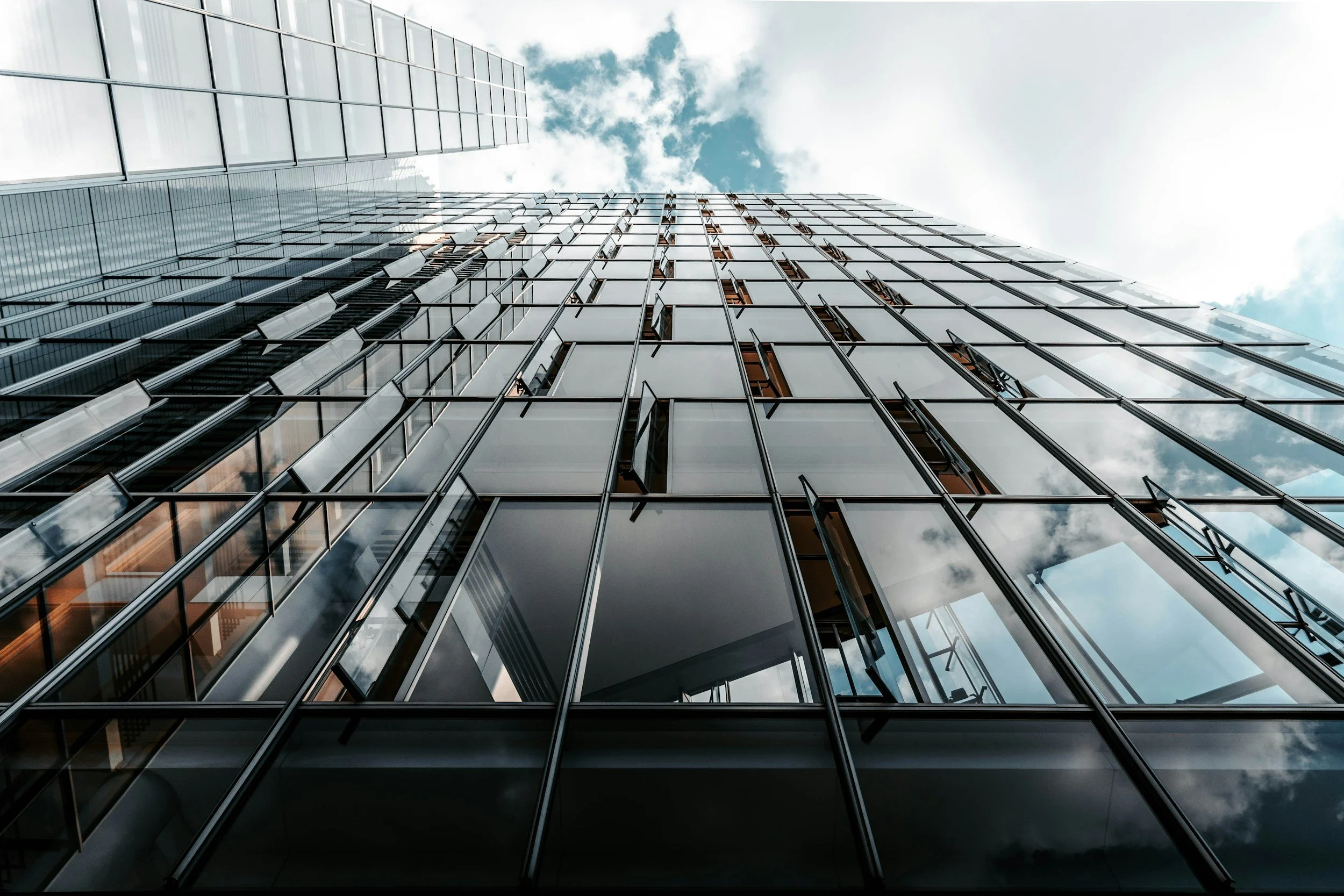 Looking up at a modern glass high-rise building with reflective windows and a blue sky with clouds above.